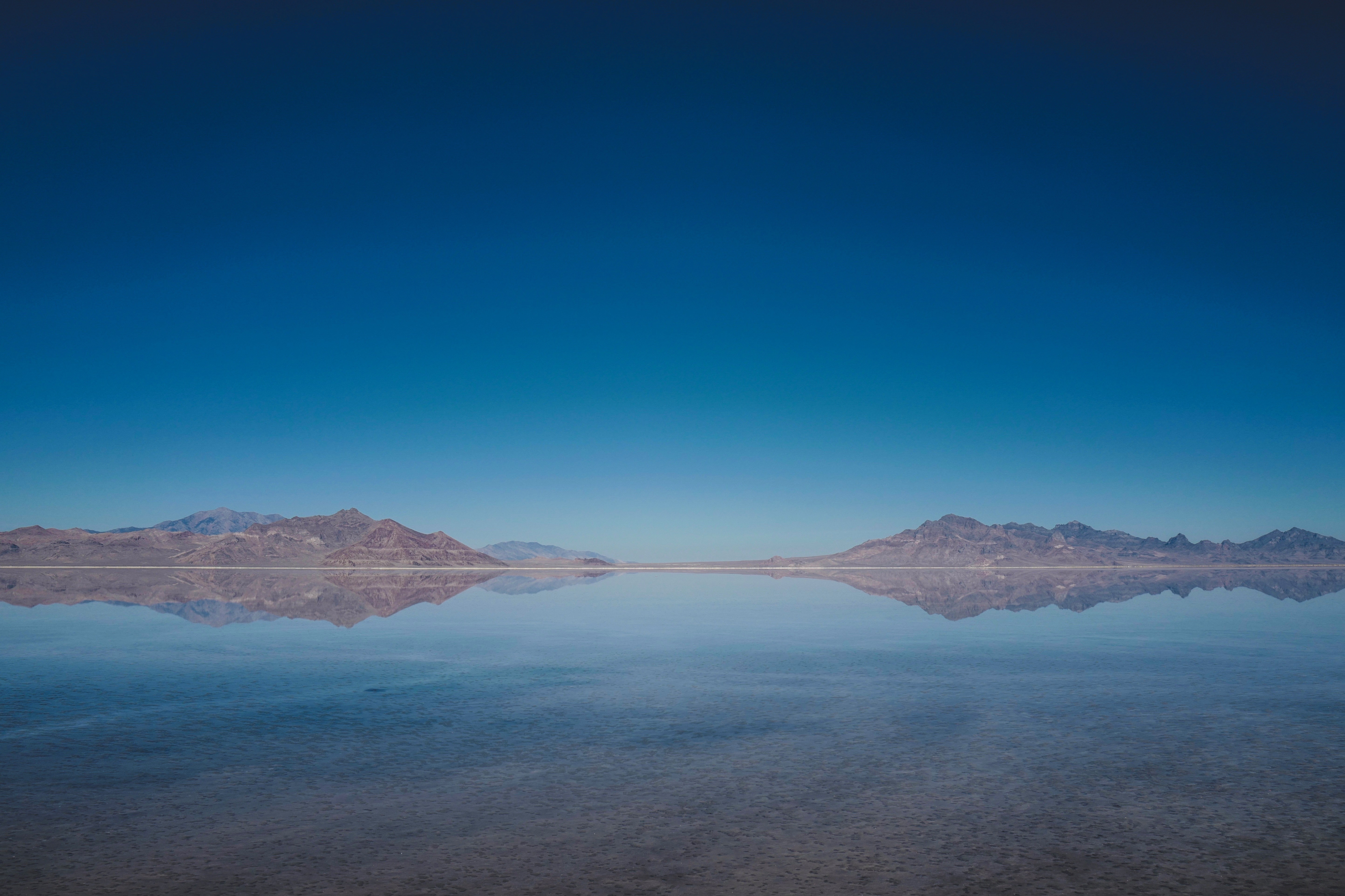 Mountains reflected in a calm body of water under a clear blue sky HD Wallpaper