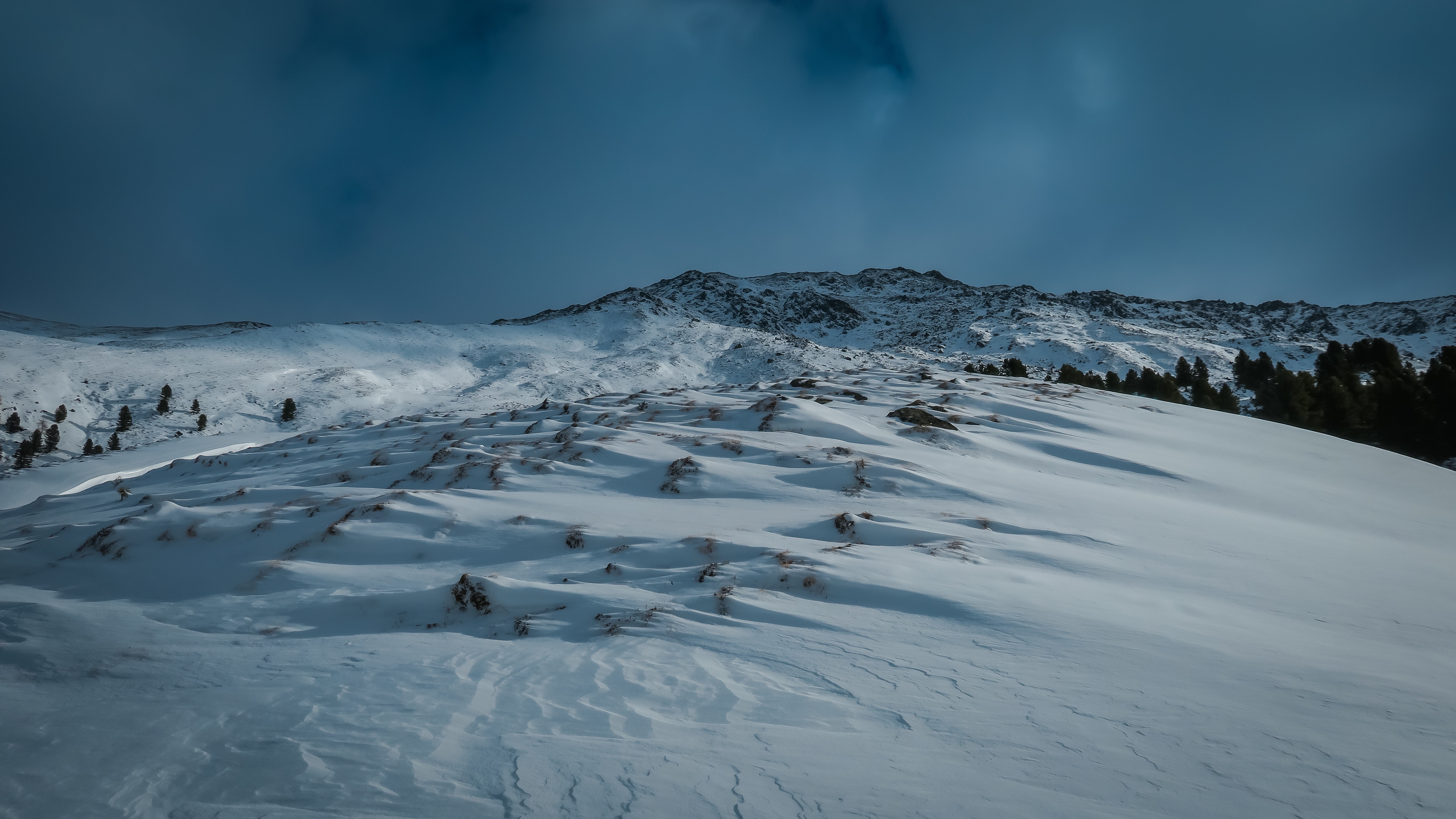 Snowy mountain landscape with pine trees under a dark sky HD Wallpaper
