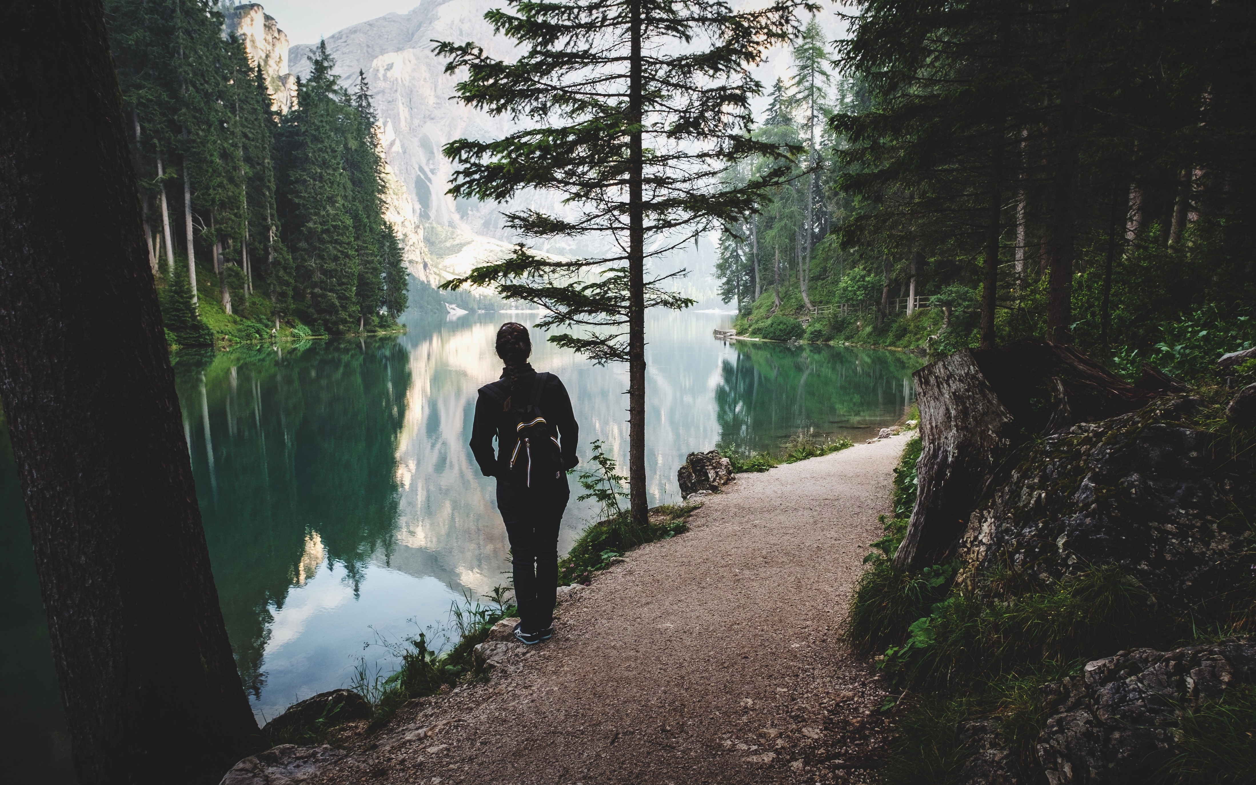 Person walking on a trail by a lake in the mountains HD Wallpaper