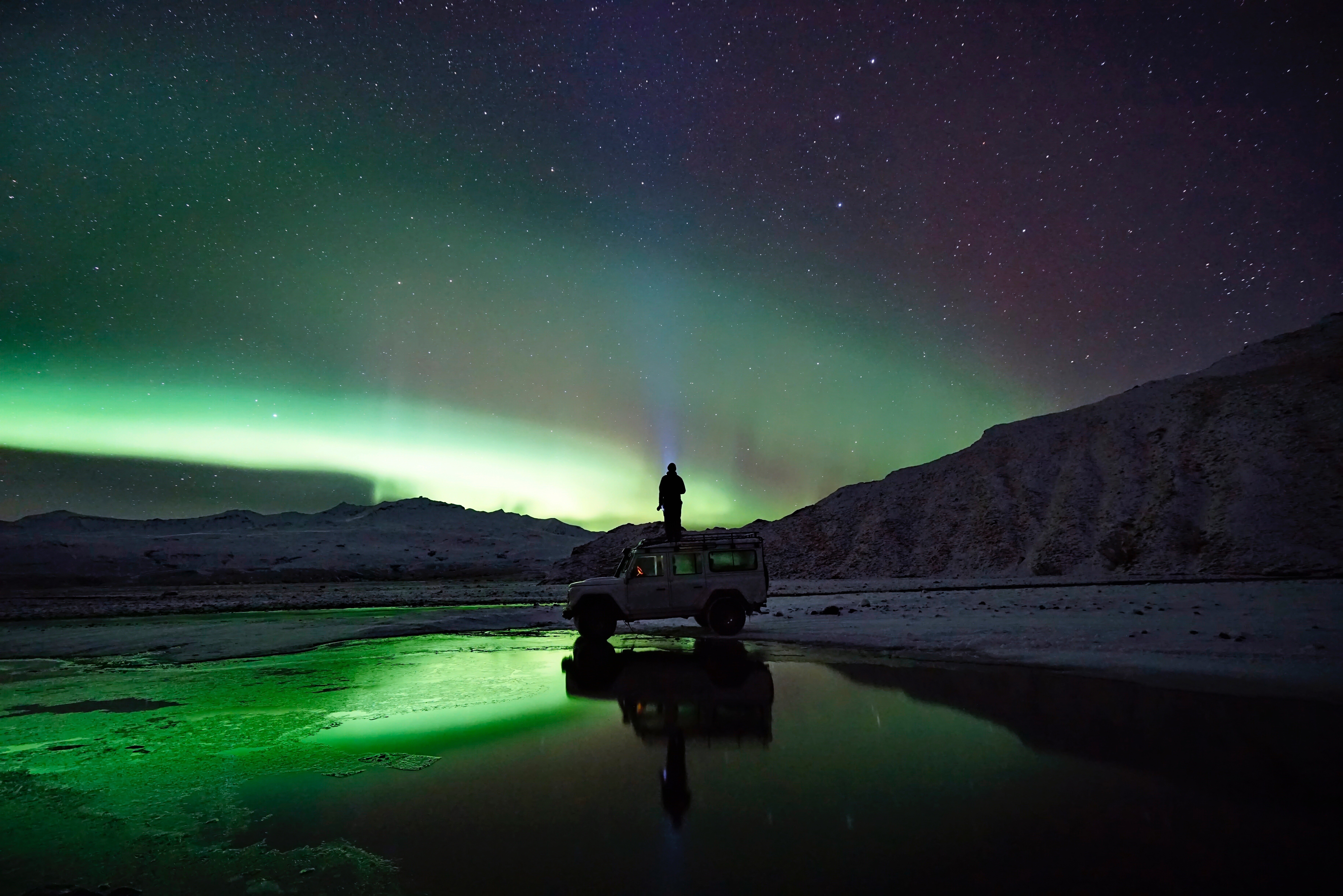 Person on car under Aurora Borealis with reflection HD Wallpaper