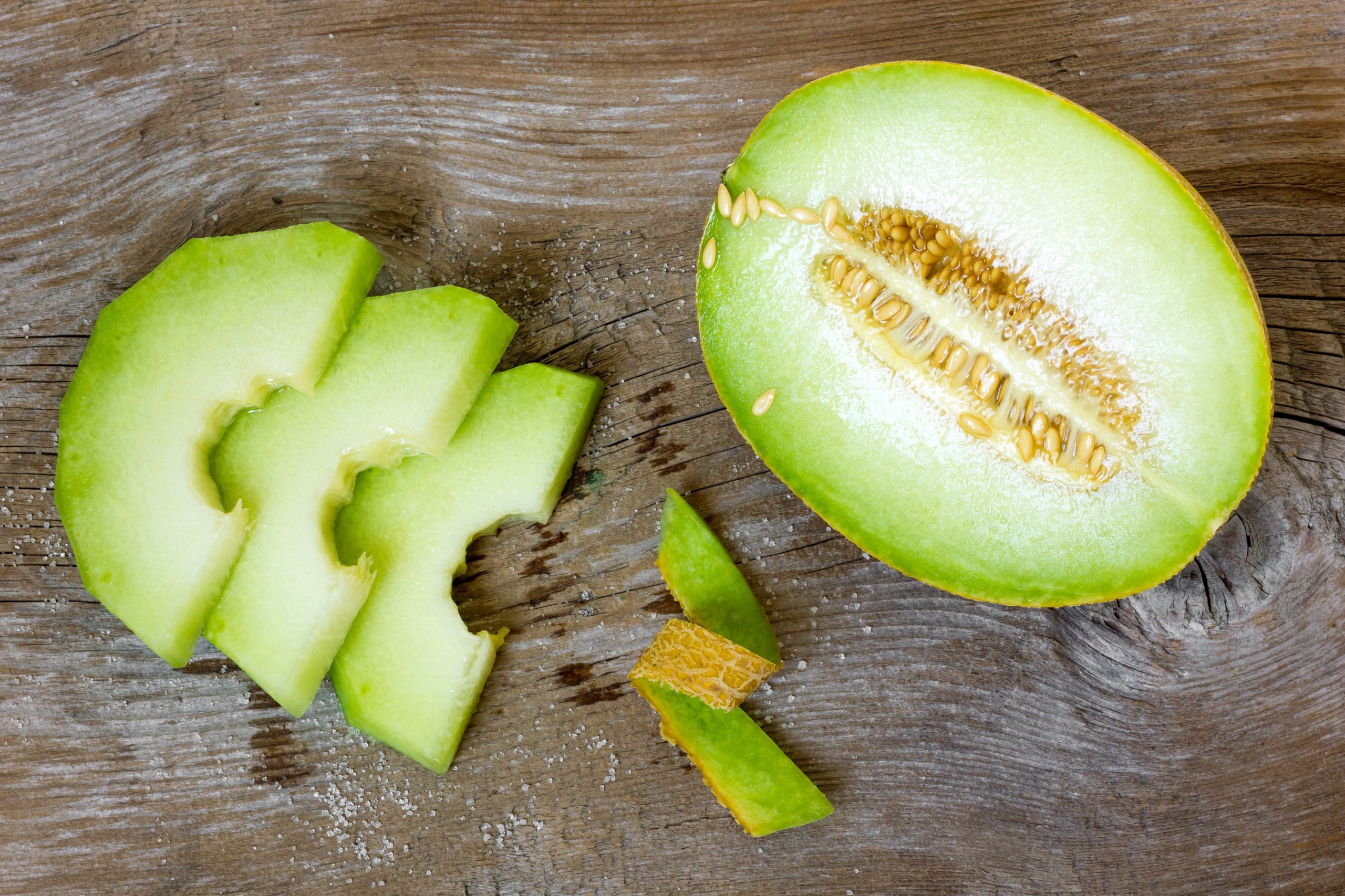 Honeydew melon cut in half with slices on a wooden table HD Wallpaper