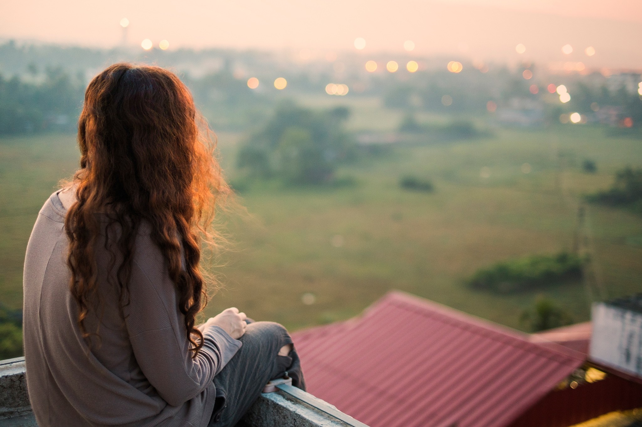 Woman with wavy hair sitting on a rooftop at sunset HD Wallpaper