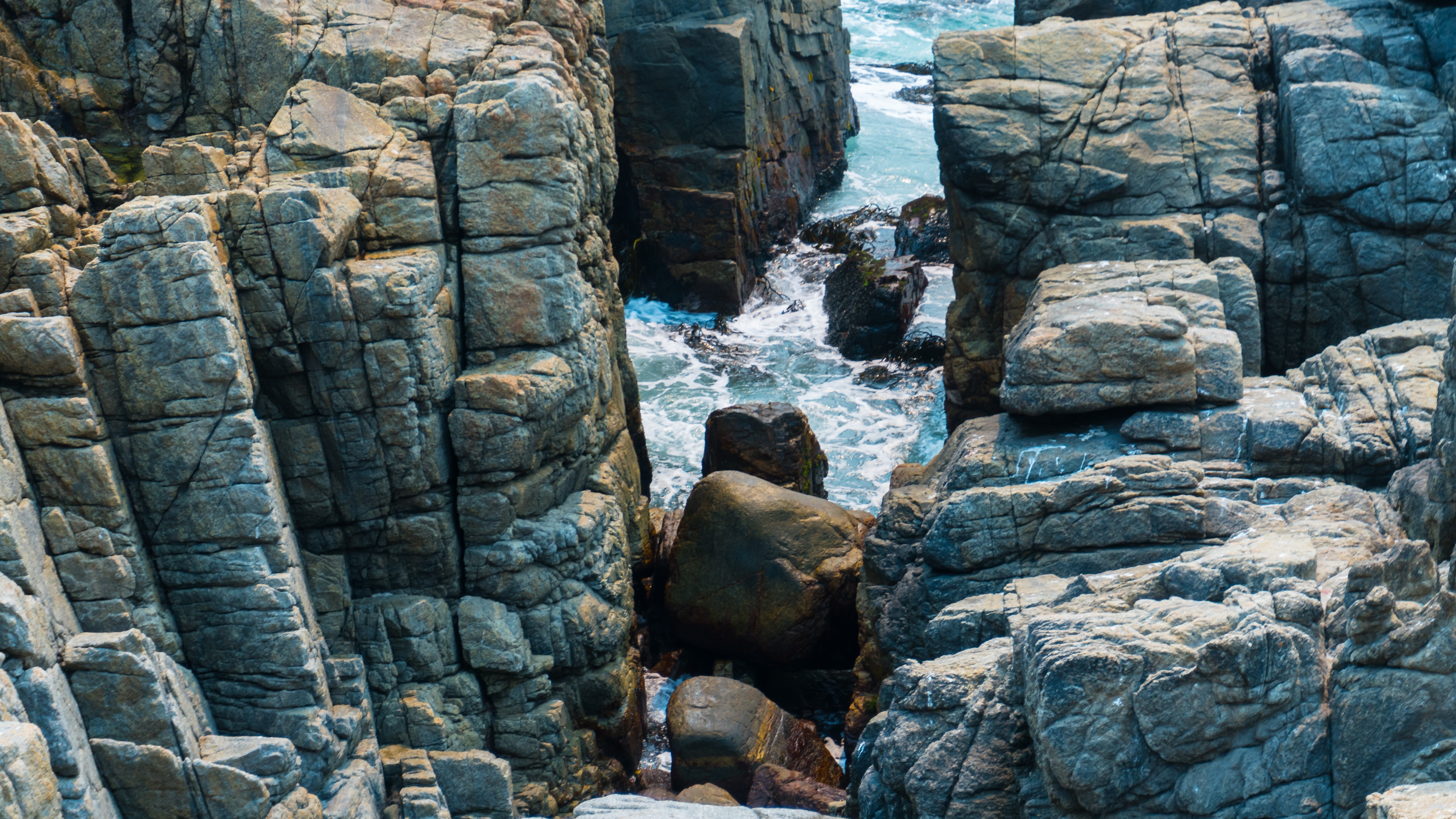 Rocky coastline with waves crashing against boulders HD Wallpaper