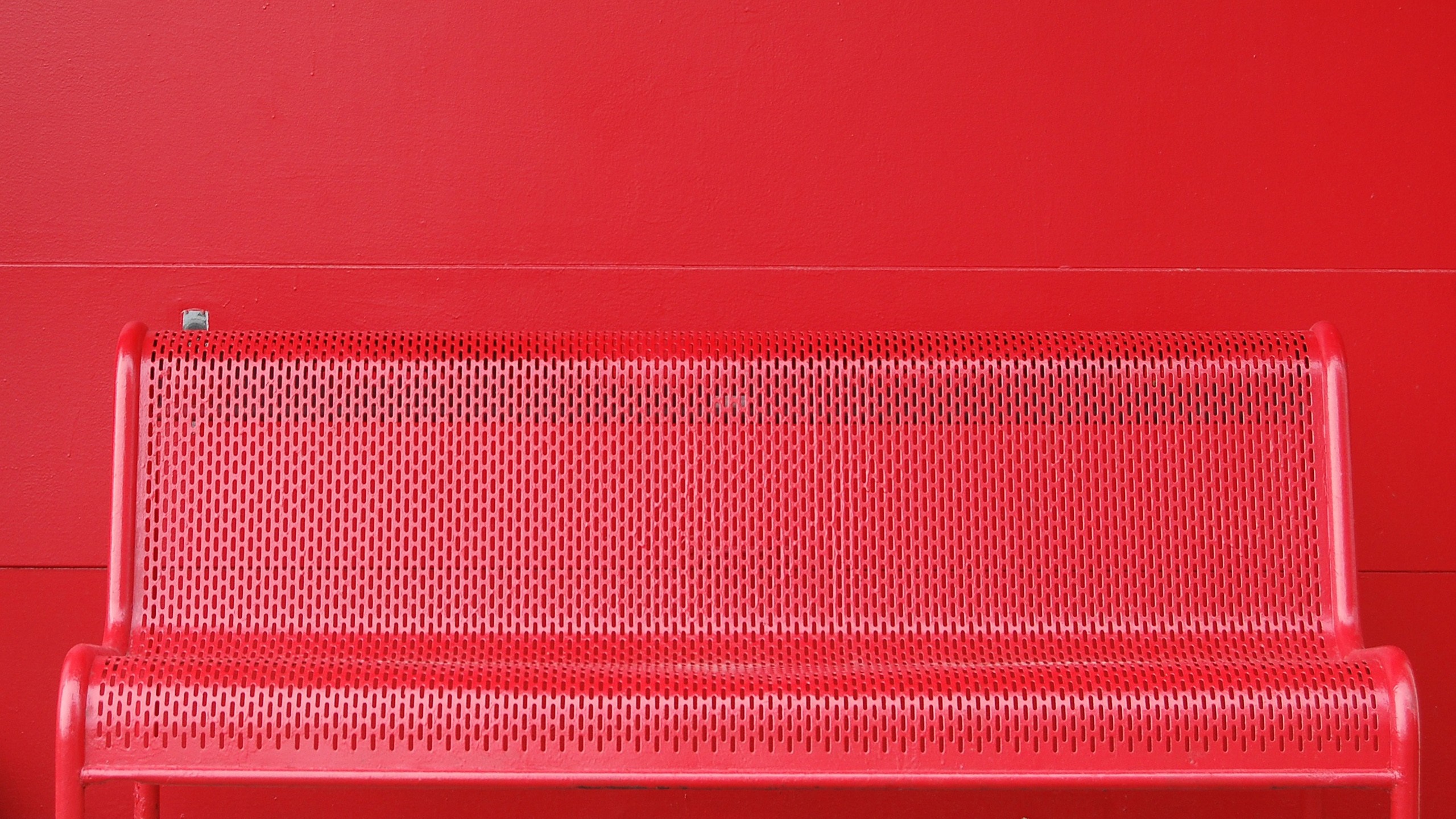 Red perforated bench against a red wall HD Wallpaper