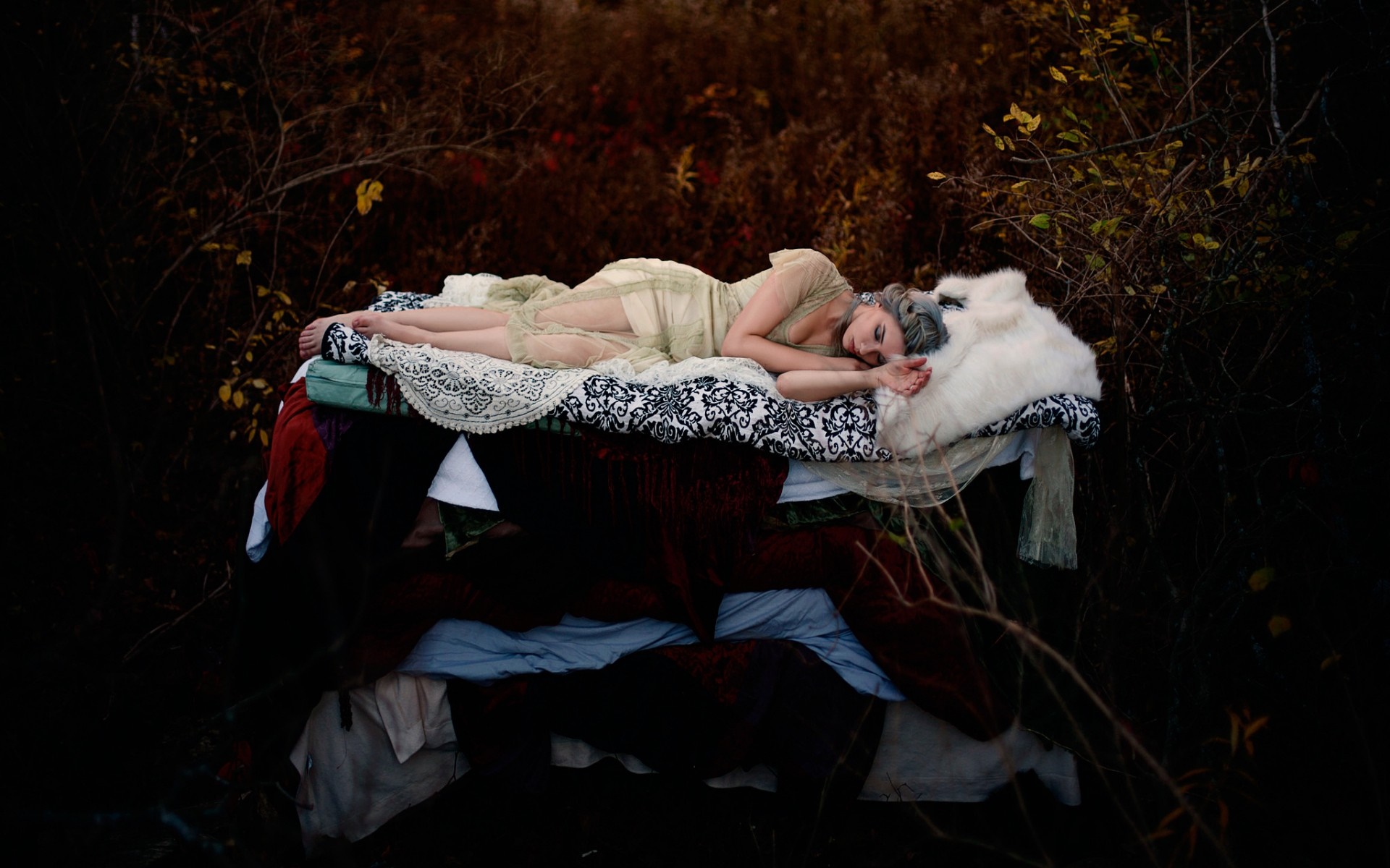 Woman sleeping on a bed of blankets in a dark forest HD Wallpaper