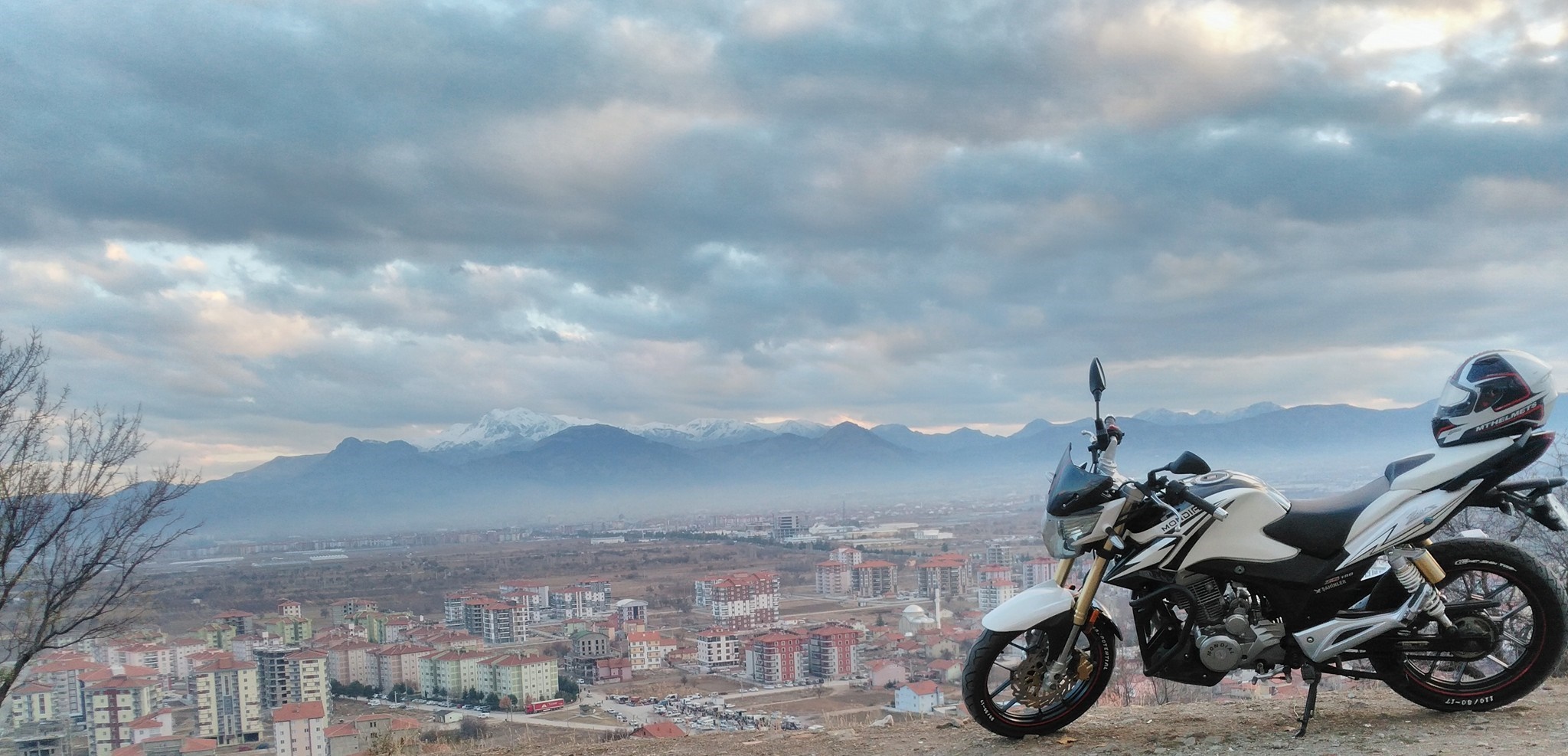 Motorcycle parked overlooking a cityscape and mountains HD Wallpaper