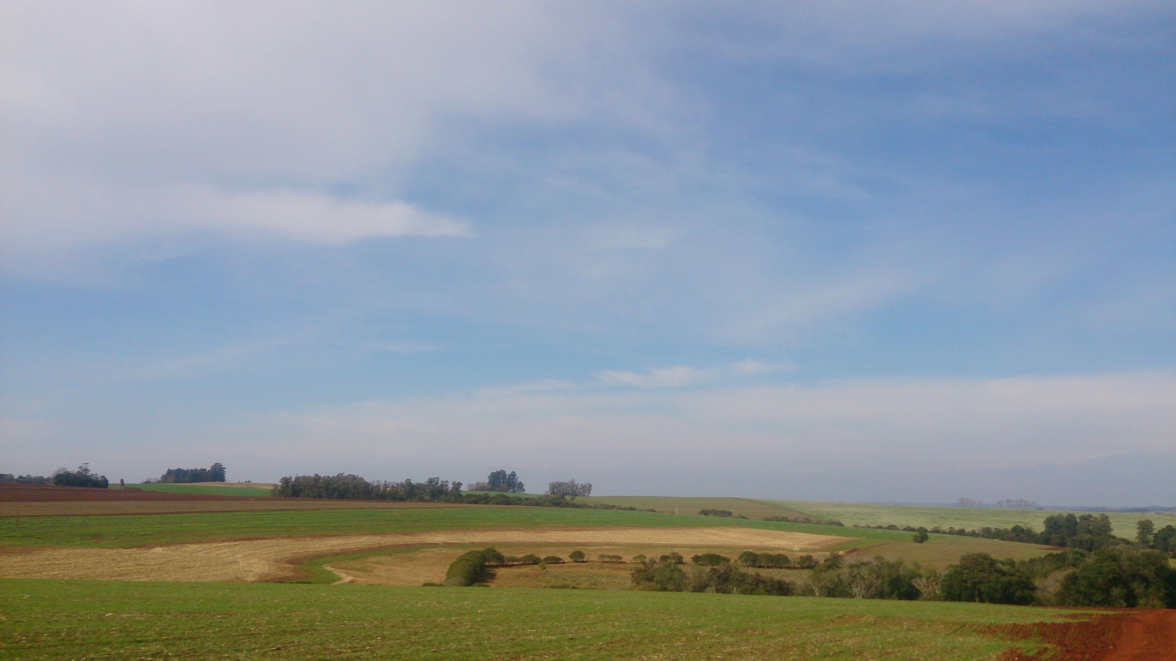 Rolling hills and agricultural fields under a cloudy sky HD Wallpaper