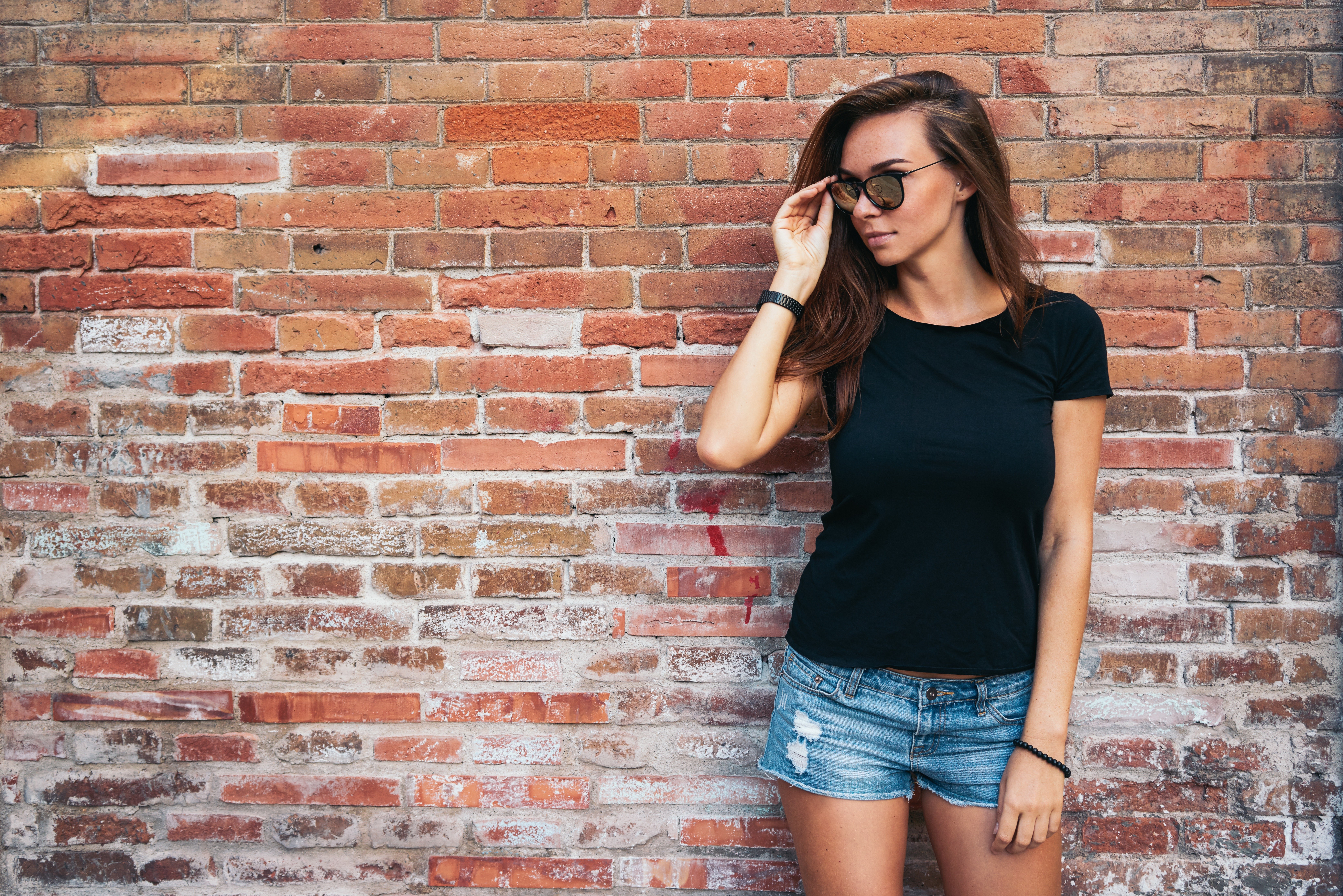 Girl in sunglasses and denim shorts against brick wall HD Wallpaper