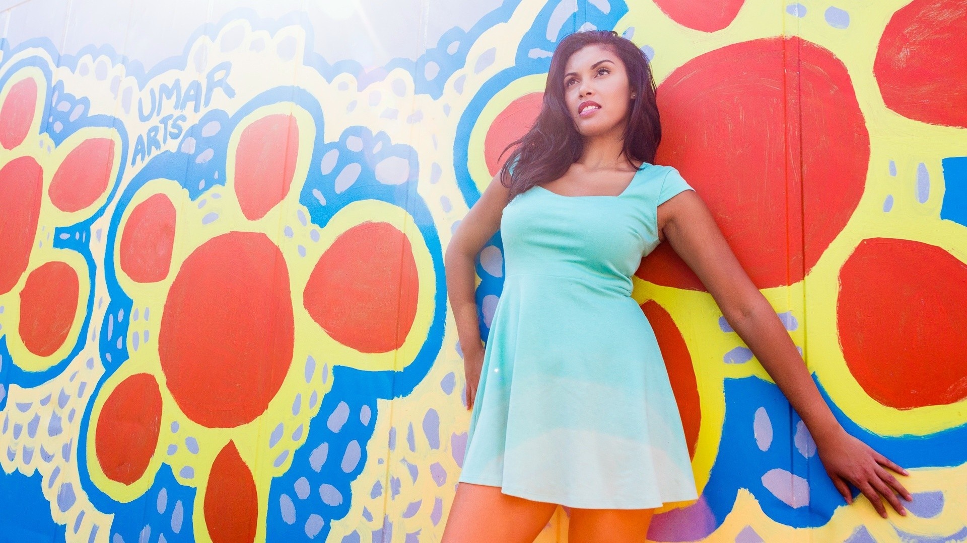 Woman in a mint green dress posing against a colorful mural HD Wallpaper