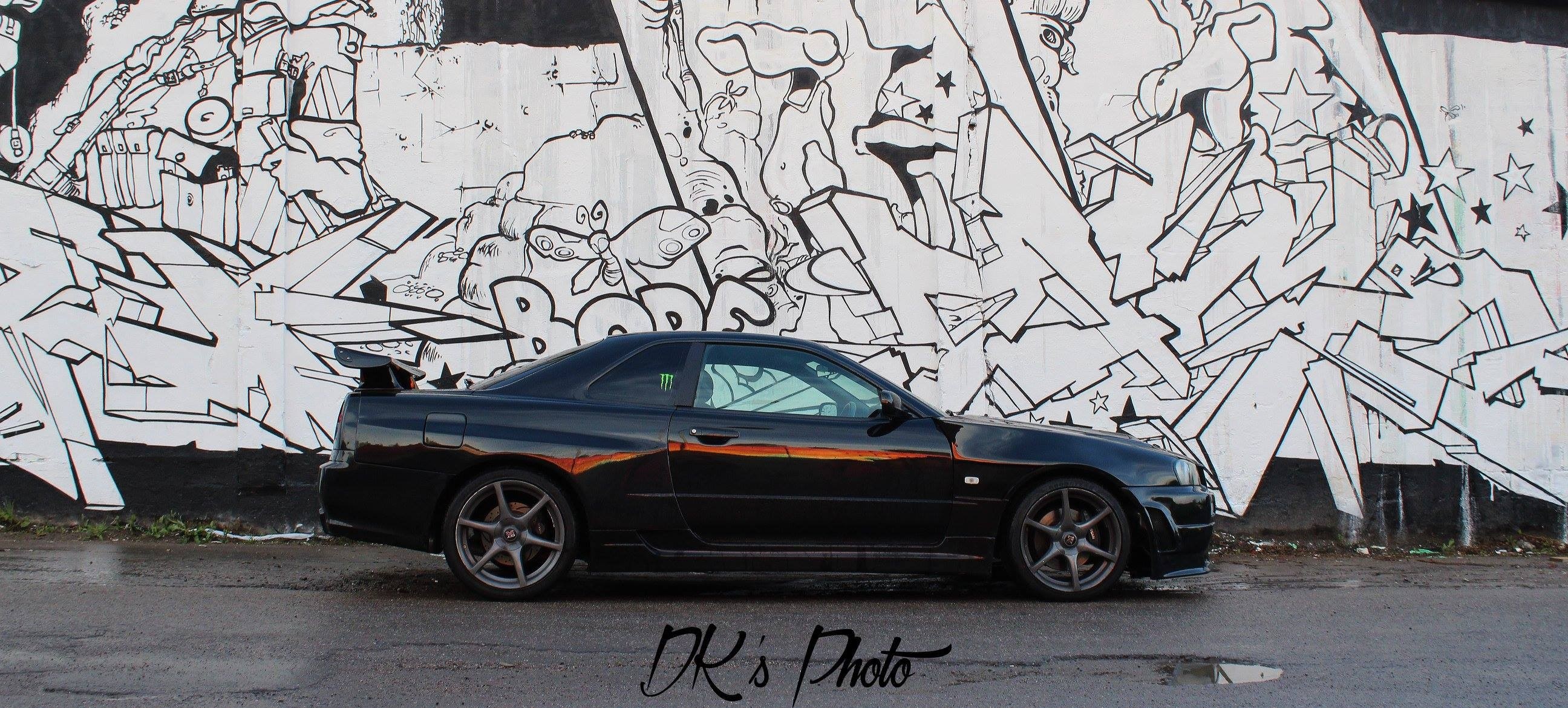 Black Nissan Skyline GT-R R34 parked in front of graffiti wall HD Wallpaper