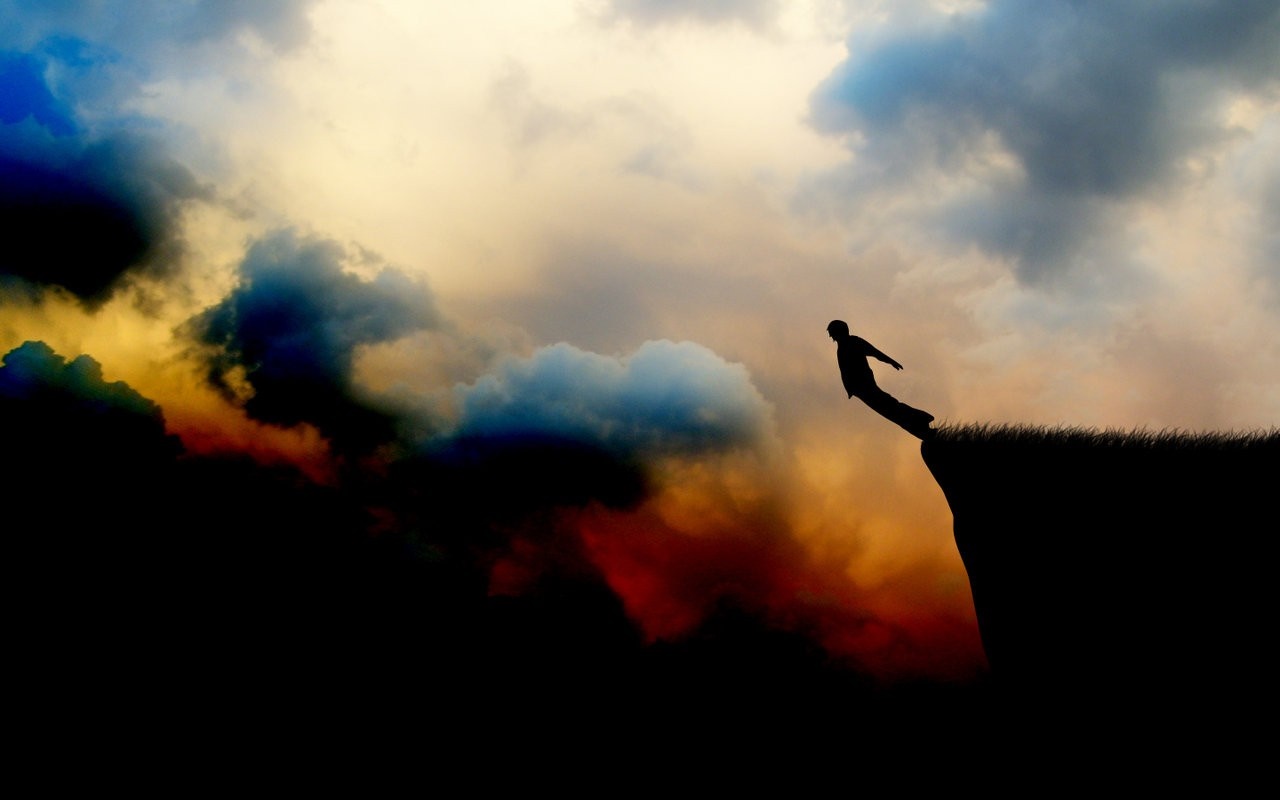 Silhouette of a person jumping off a cliff at sunset HD Wallpaper