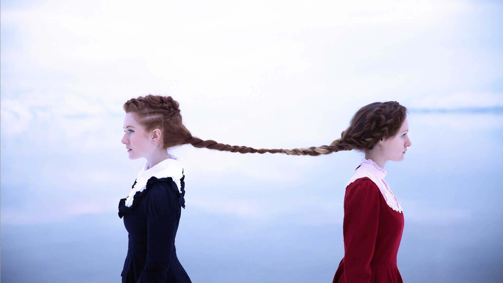 Two women with braided hair connected by braids outdoors HD Wallpaper