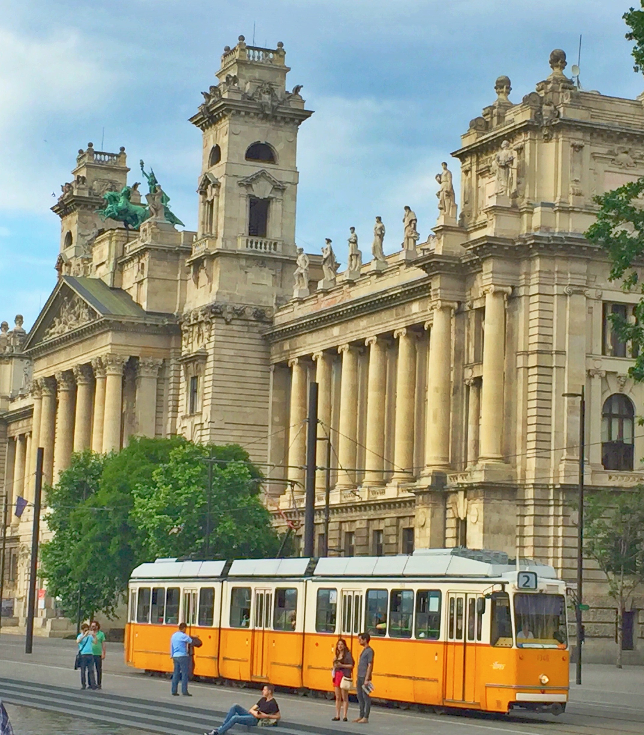 Orange tram in front of a grand building in Budapest, Hungary HD Wallpaper