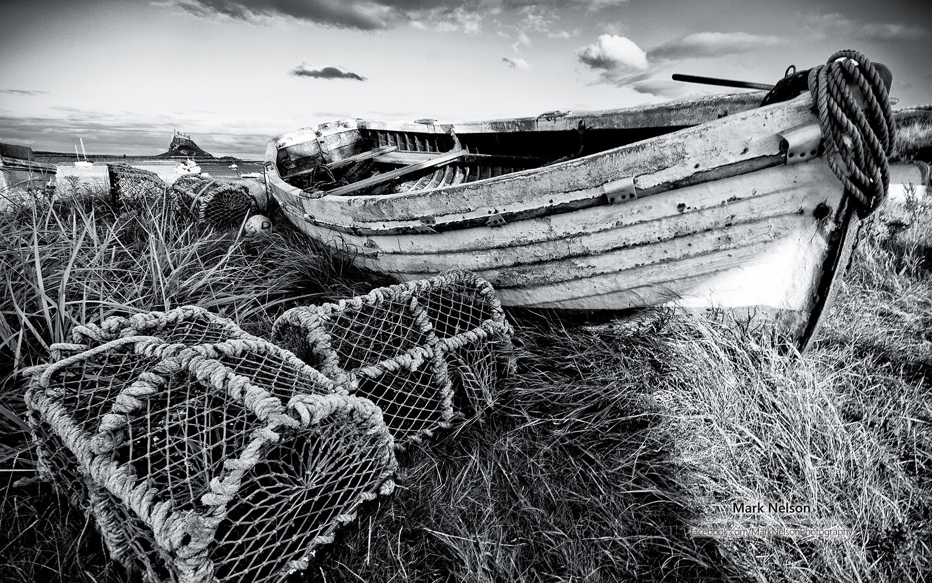 Abandoned boat and lobster pots on grassy shore with castle in distance HD Wallpaper