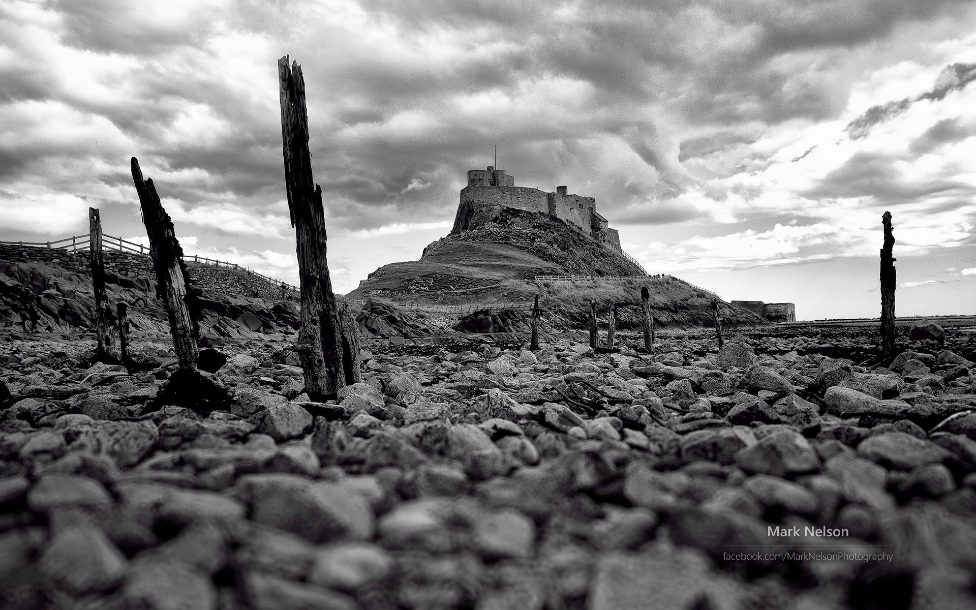 Lindisfarne Castle on a rocky shore with wooden posts HD Wallpaper
