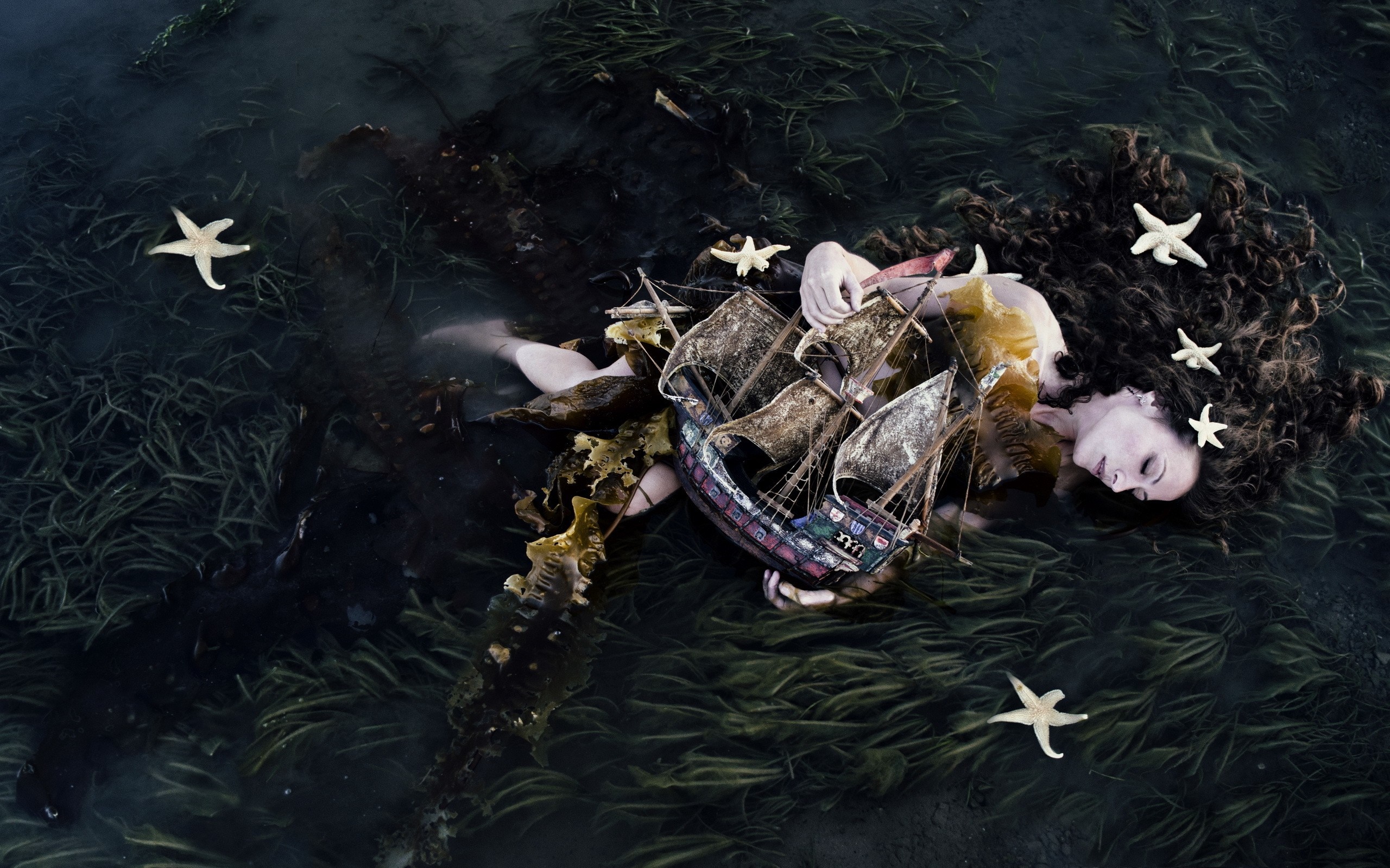 Woman with a model ship in dark water with seaweed and starfish HD Wallpaper