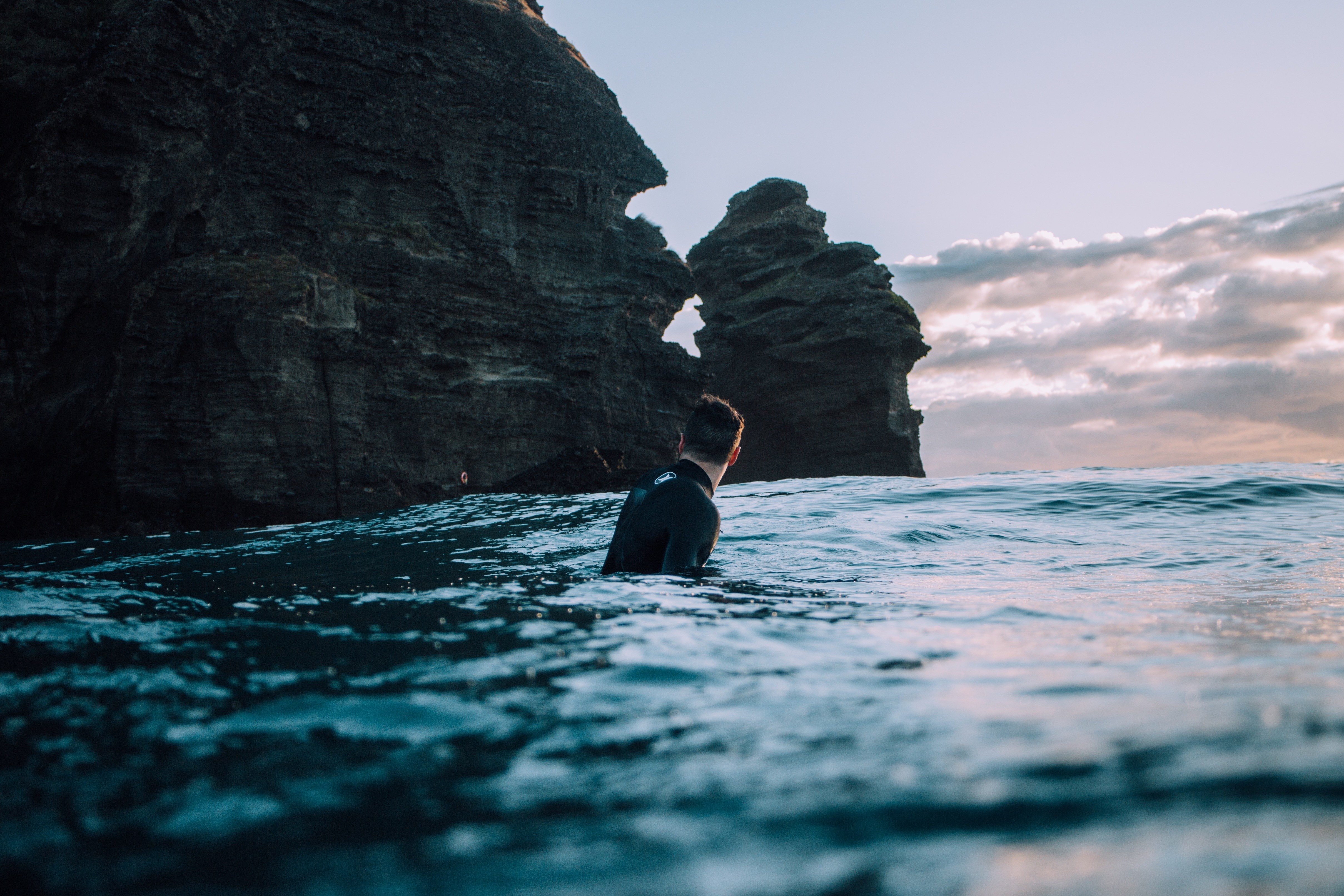 Surfer in wetsuit in ocean near rocky cliffs HD Wallpaper