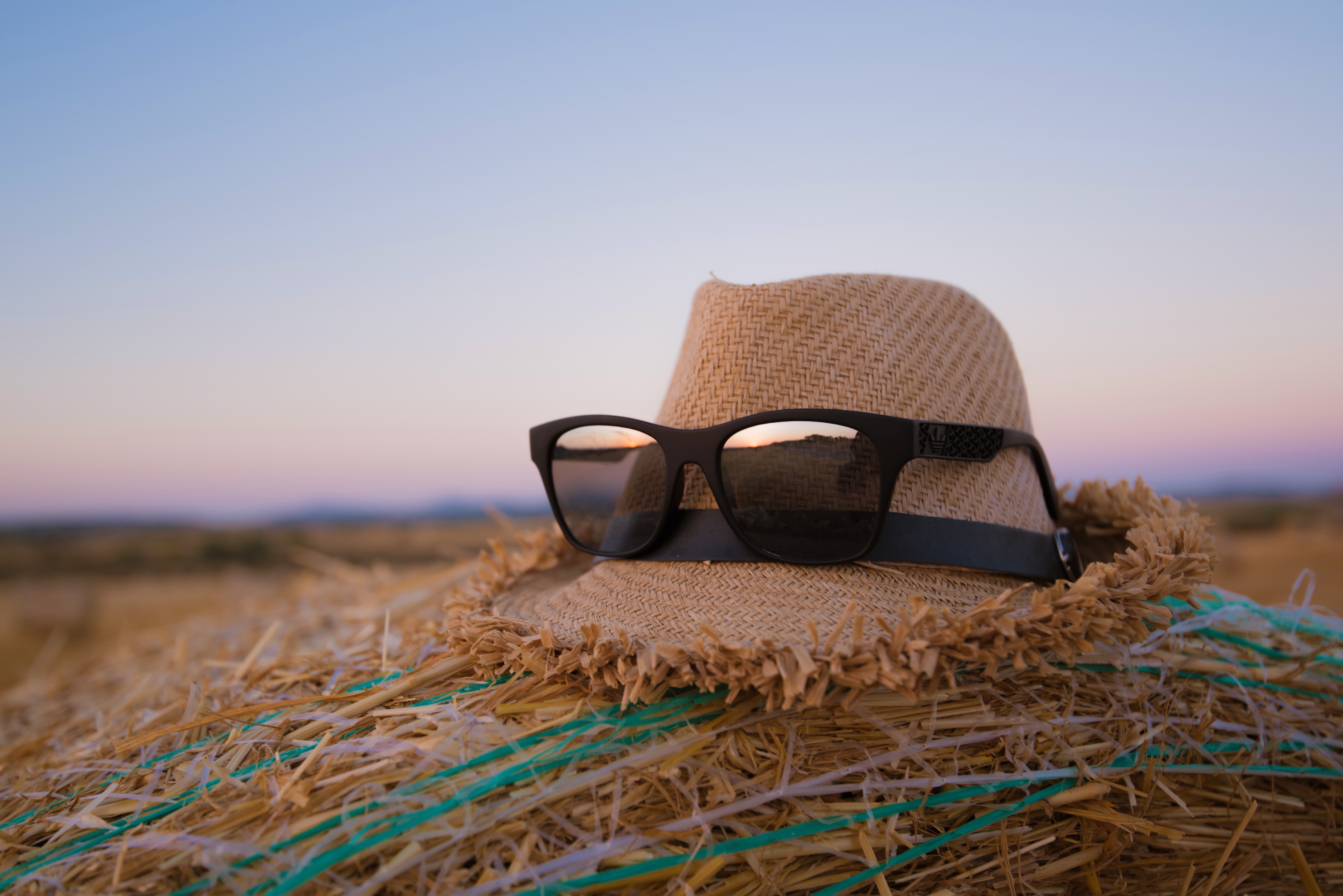 Straw hat and sunglasses on a hay bale at sunset HD Wallpaper