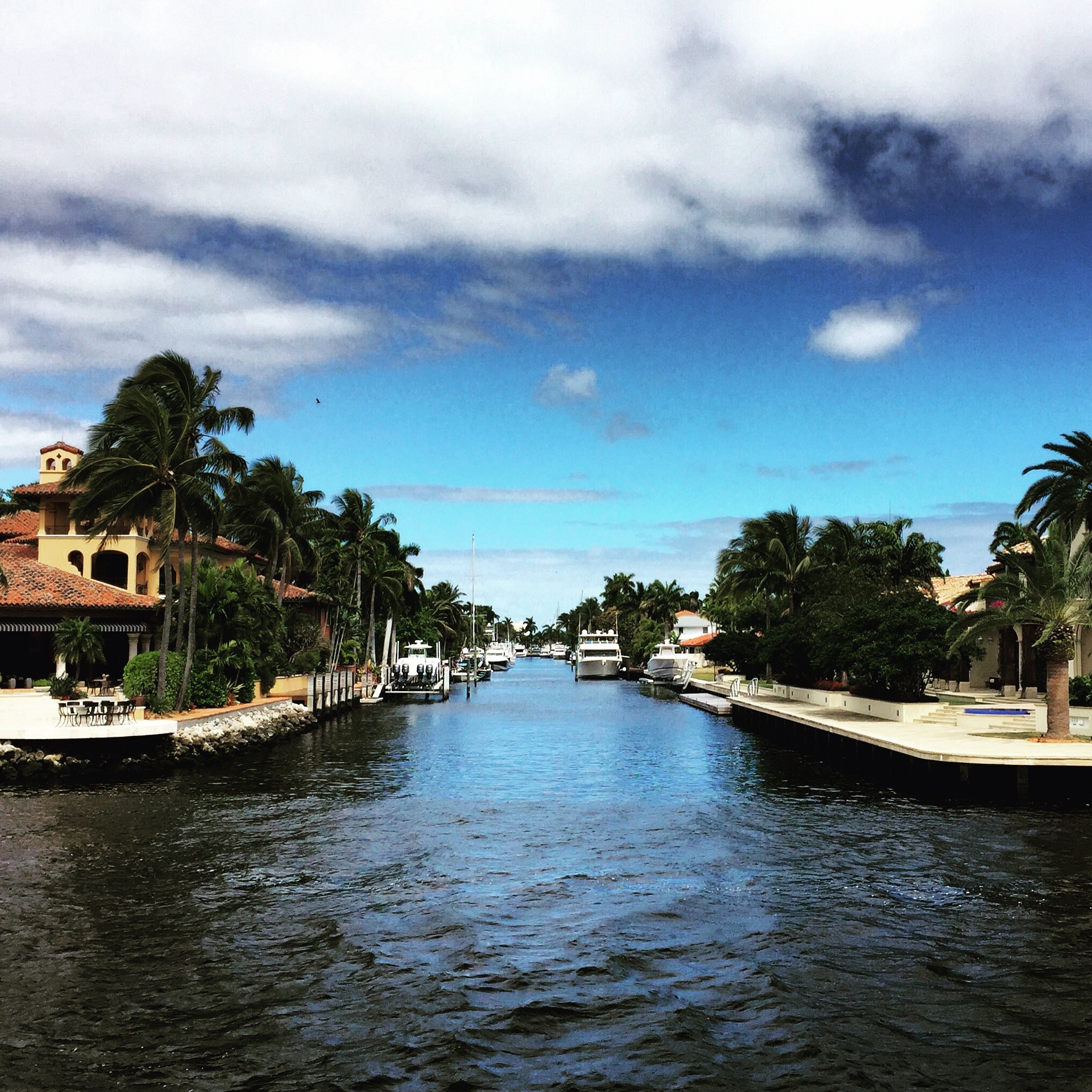 Luxury canal homes with yachts under a cloudy sky HD Wallpaper