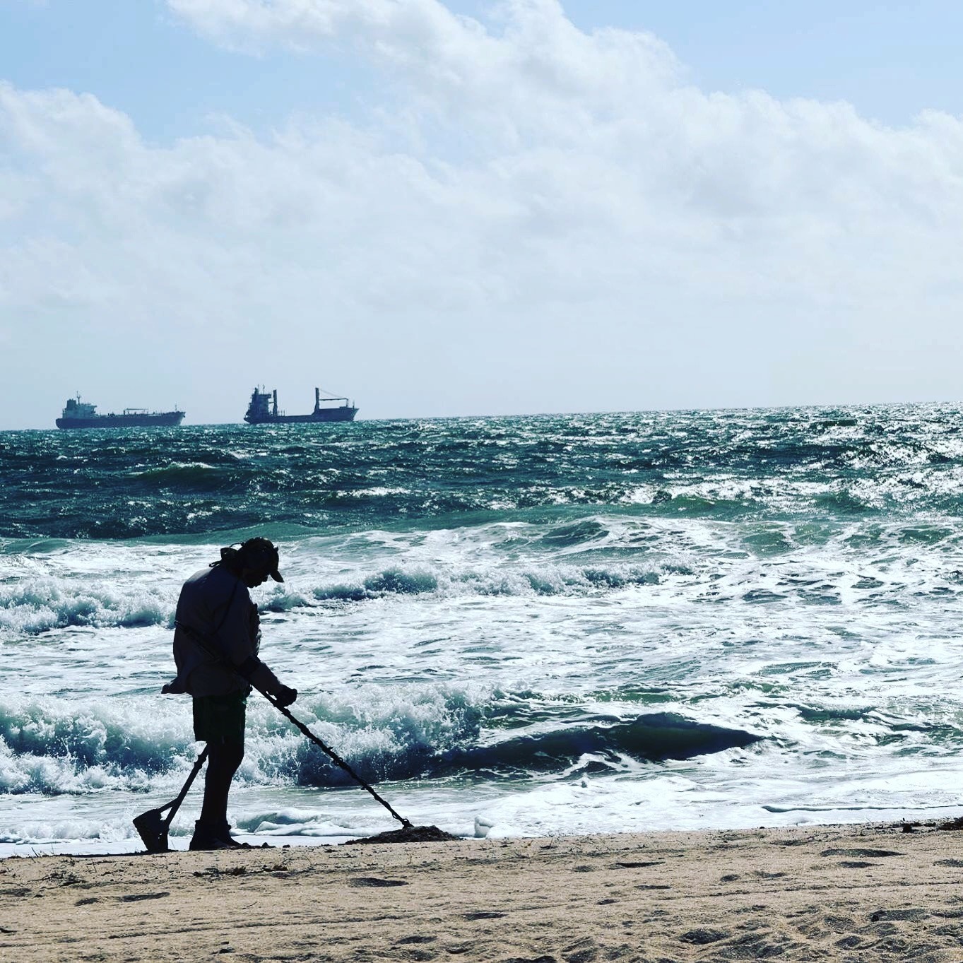 Person metal detecting on a beach with ships in the distance HD Wallpaper