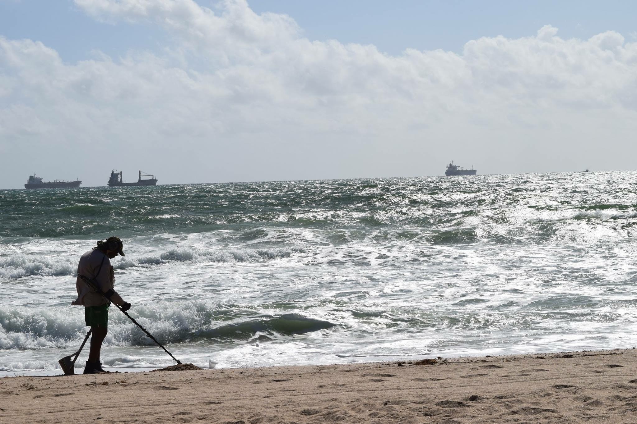 Man metal detecting on a beach with ships in the ocean HD Wallpaper