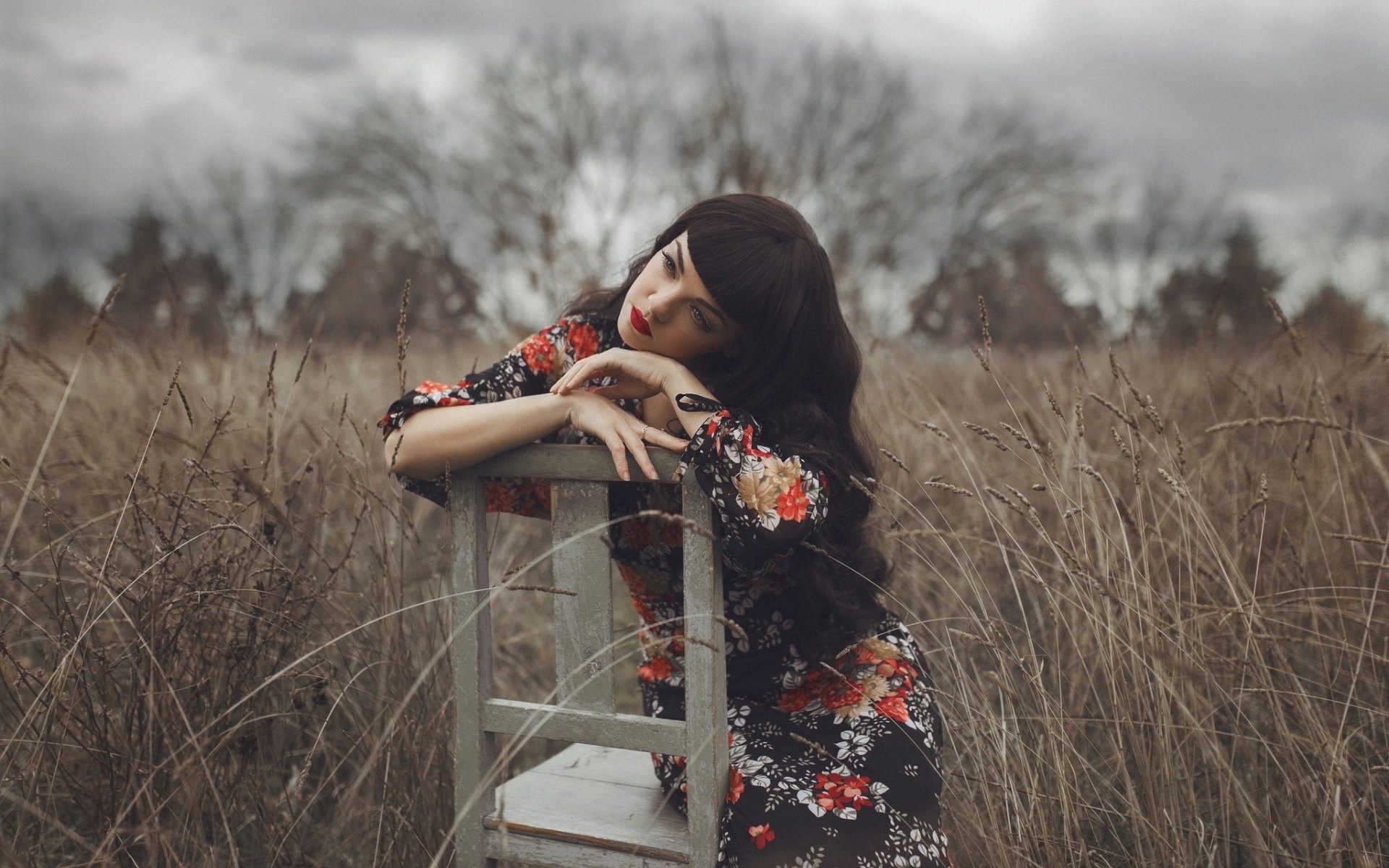 Woman in floral dress sitting on a chair in a field HD Wallpaper