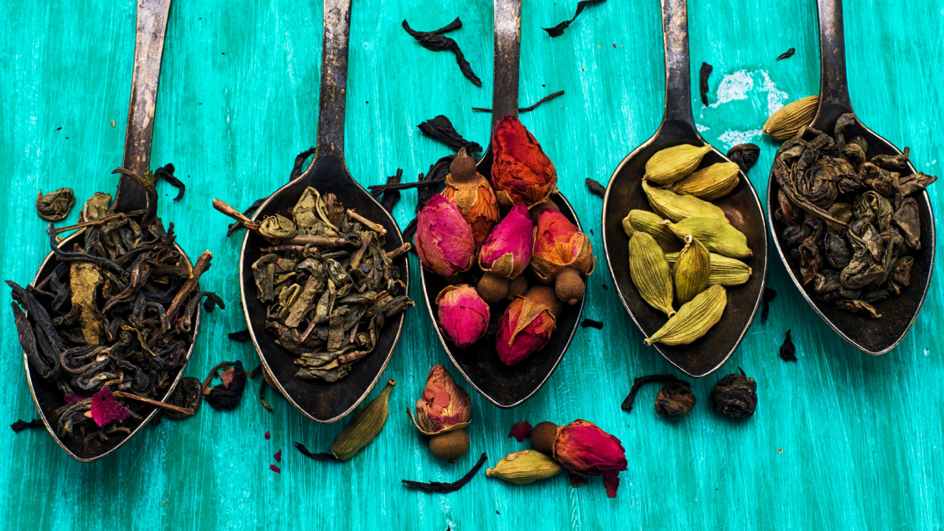Spoons filled with dried tea leaves, rose buds, and cardamom pods HD Wallpaper