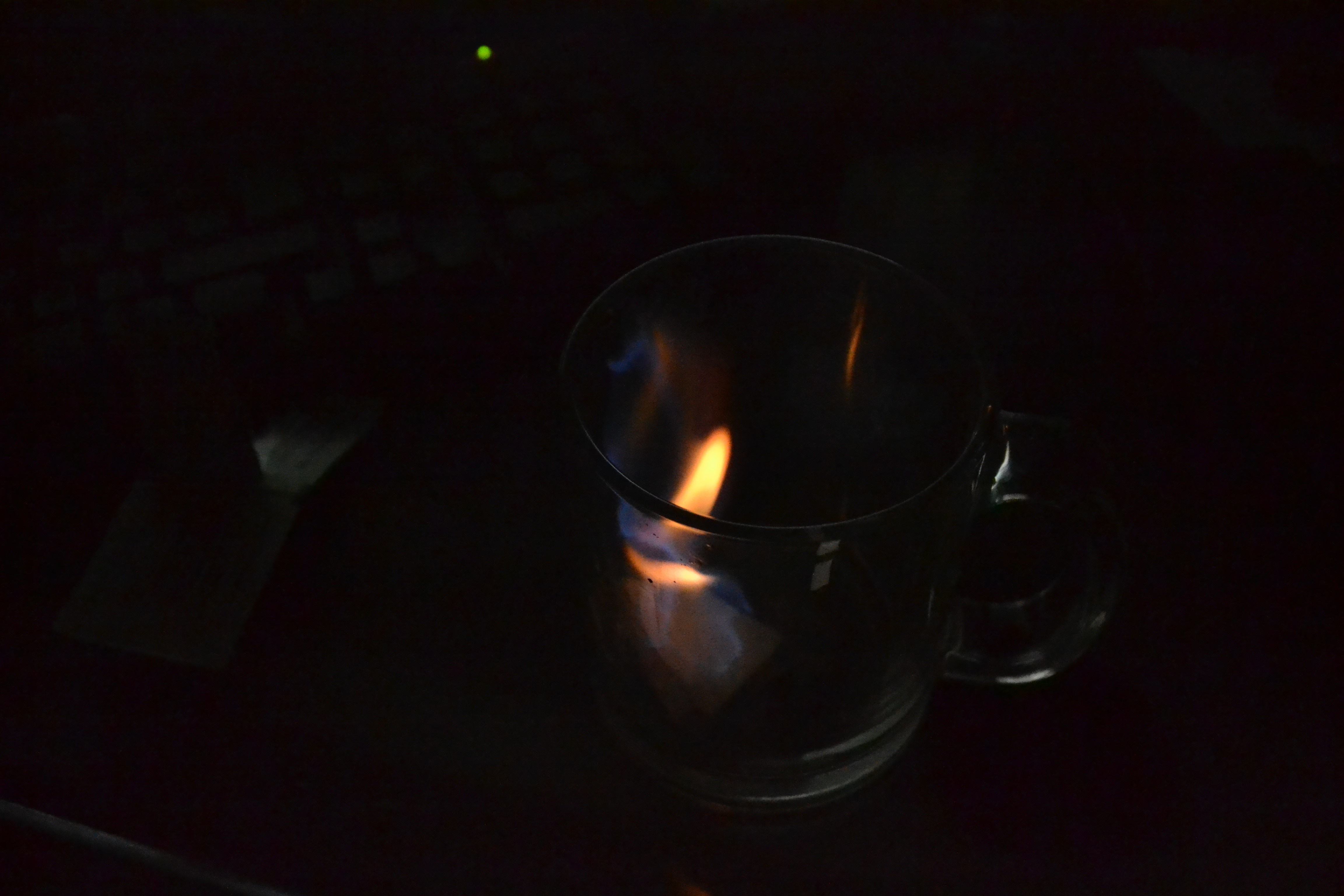 Fire burning inside a glass mug on a dark surface HD Wallpaper