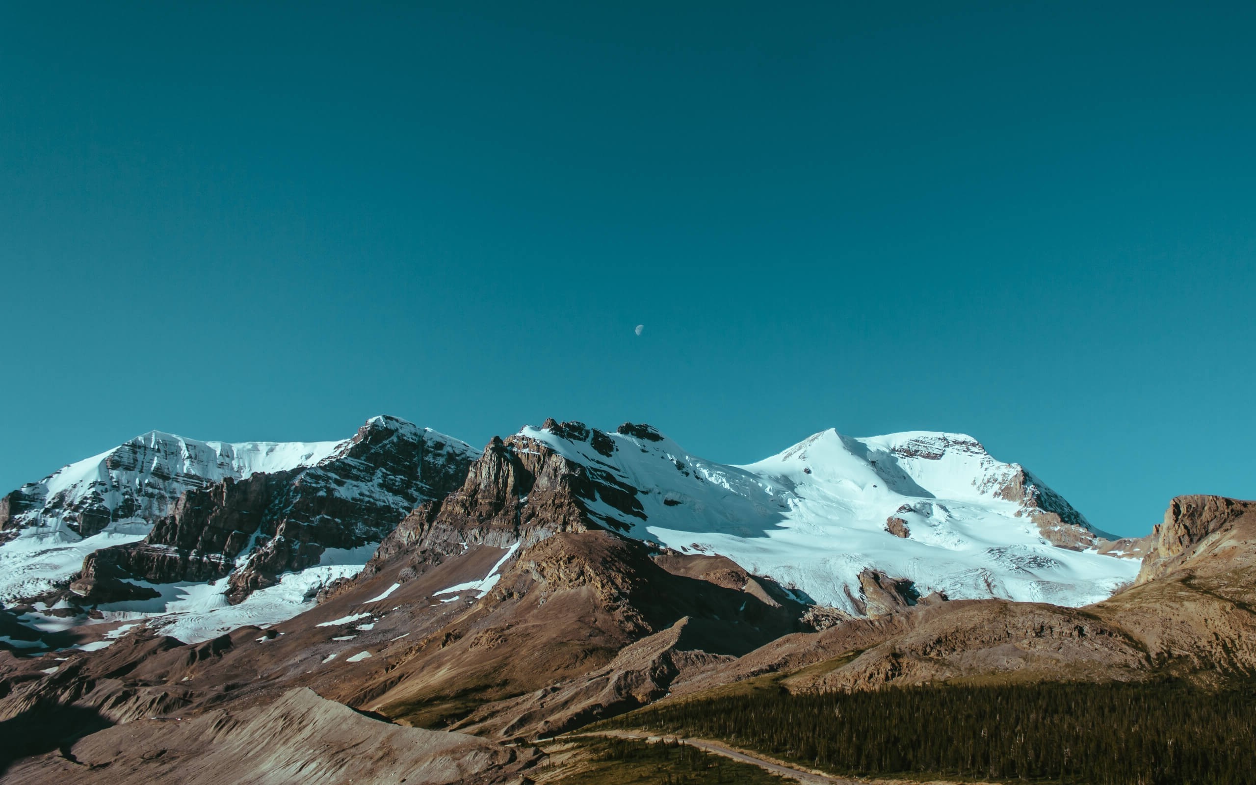 Snow-capped mountains under a clear blue sky with a crescent moon HD Wallpaper