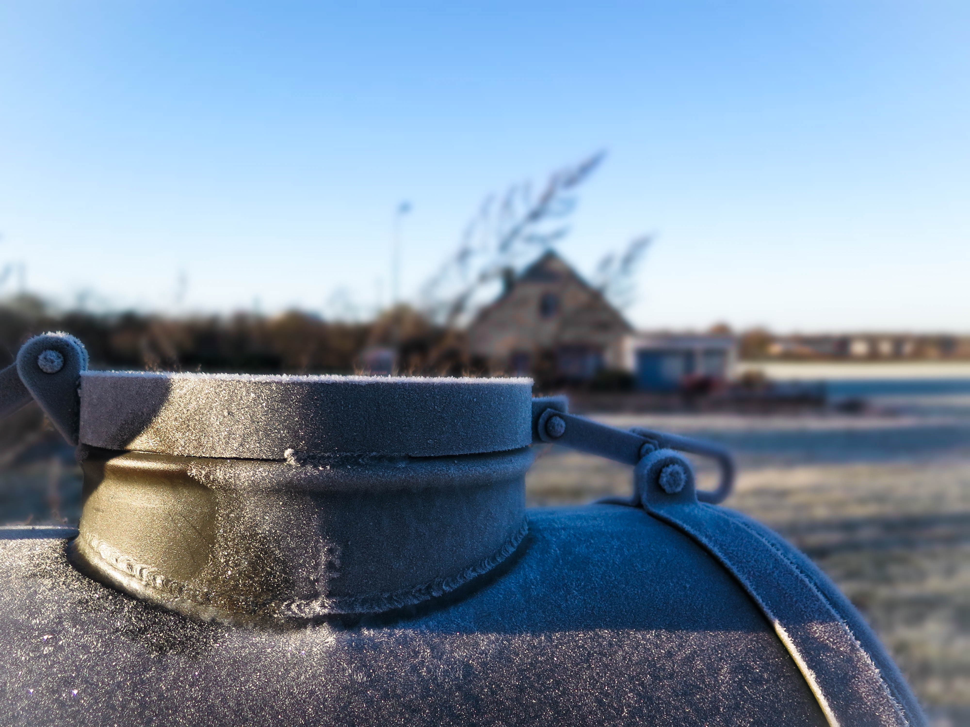 Frozen metal cap on a tank with a house in the background HD Wallpaper