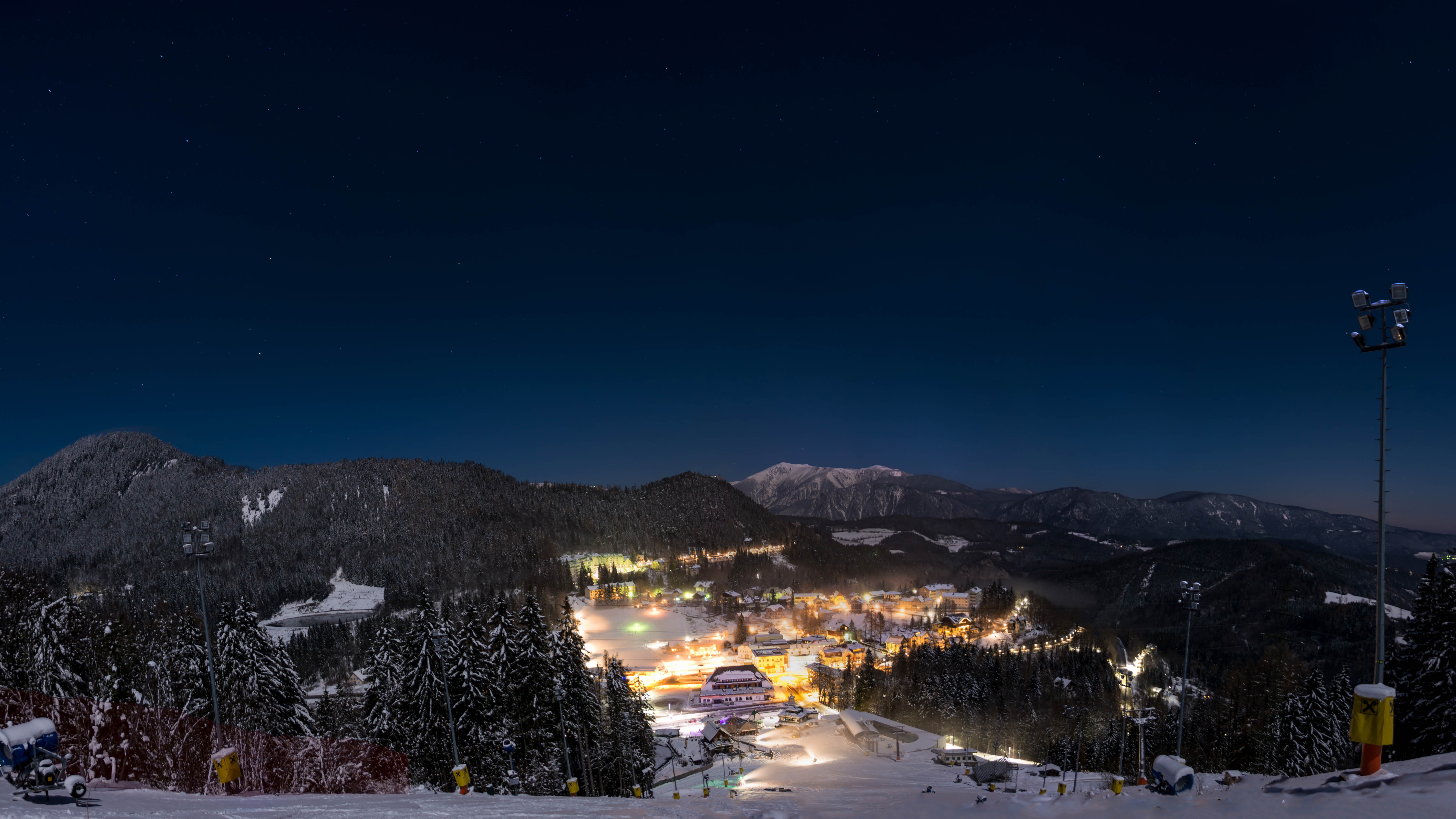 Night view of a snowy mountain resort with illuminated buildings and stars HD Wallpaper