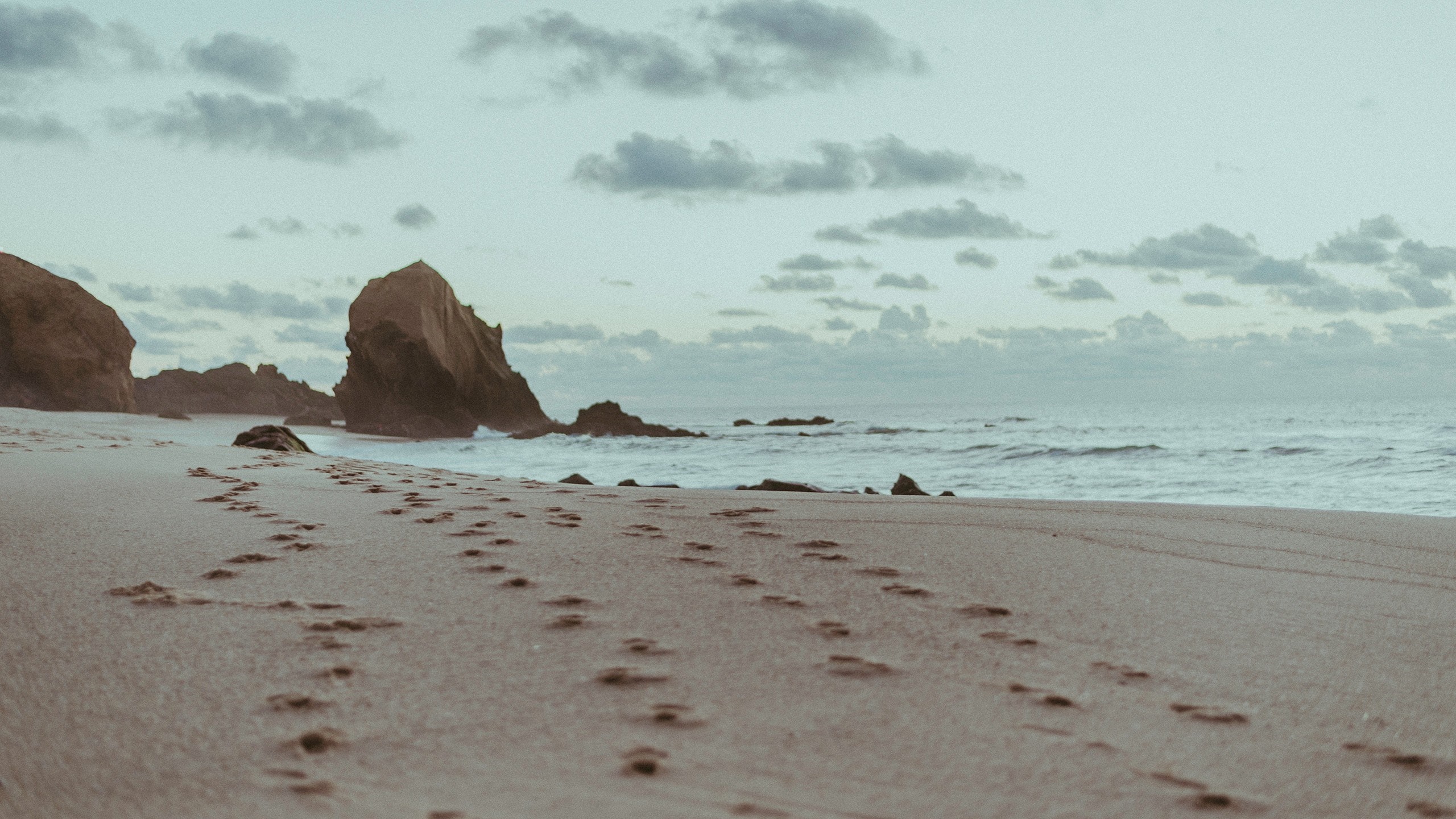 Footprints on a sandy beach with rocks and ocean waves HD Wallpaper