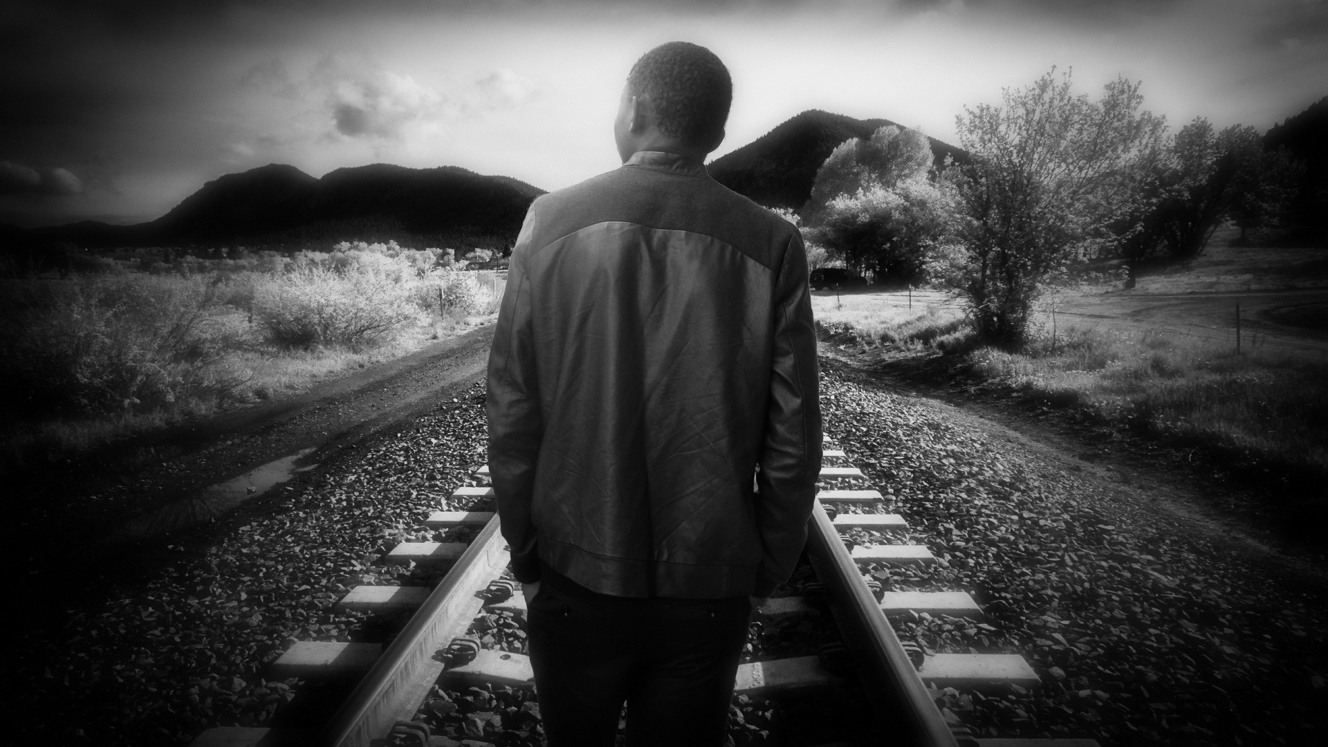 Man standing on railroad tracks in monochrome landscape HD Wallpaper