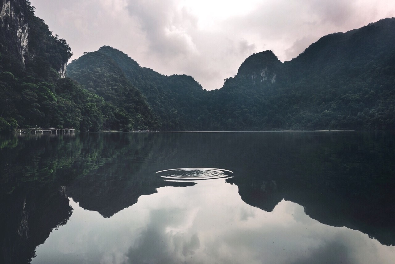 Misty mountains reflected in a calm lake with ripples HD Wallpaper