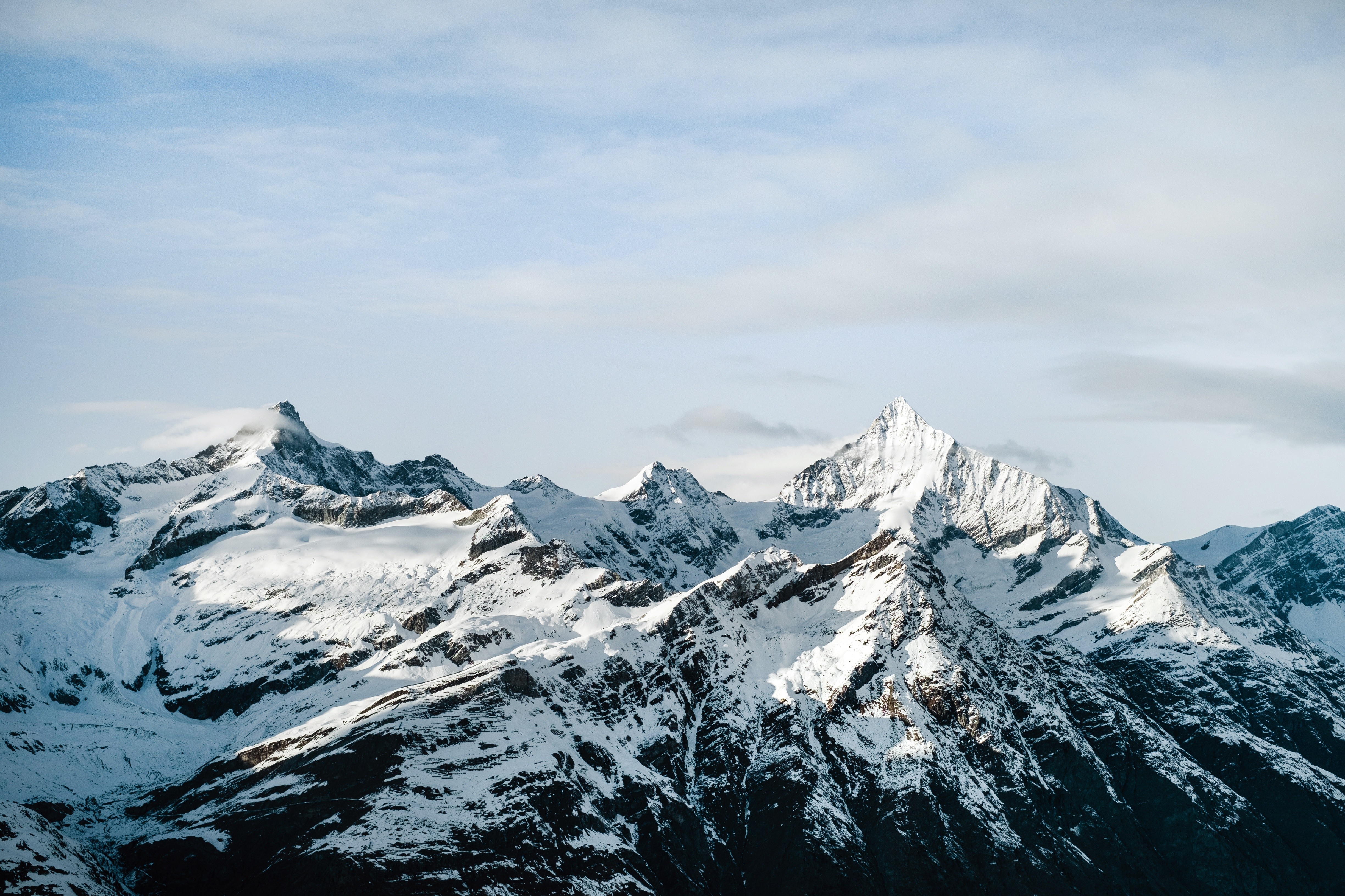 Snow-covered mountains under a cloudy sky HD Wallpaper