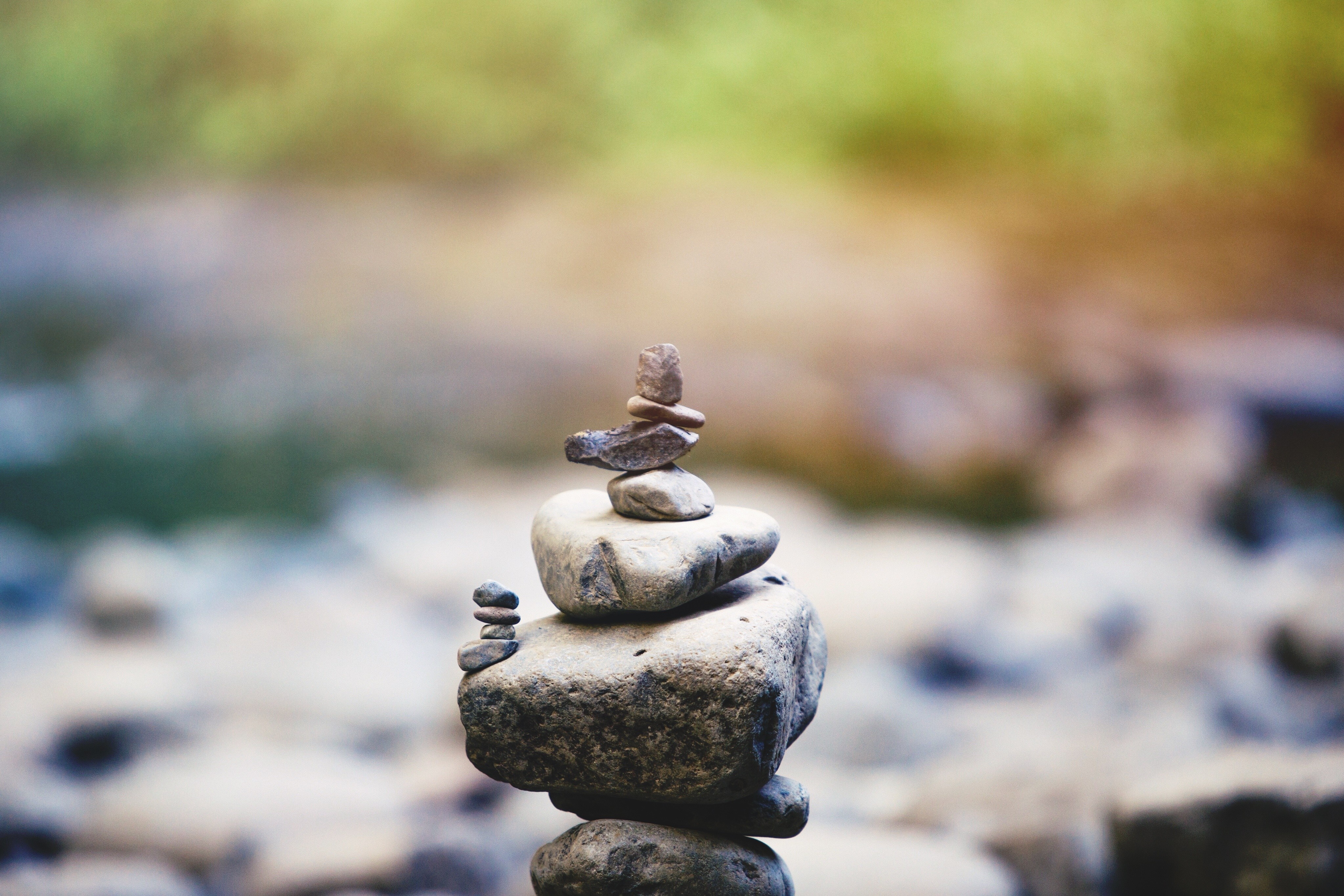 Stacked rocks in front of blurred water and foliage HD Wallpaper