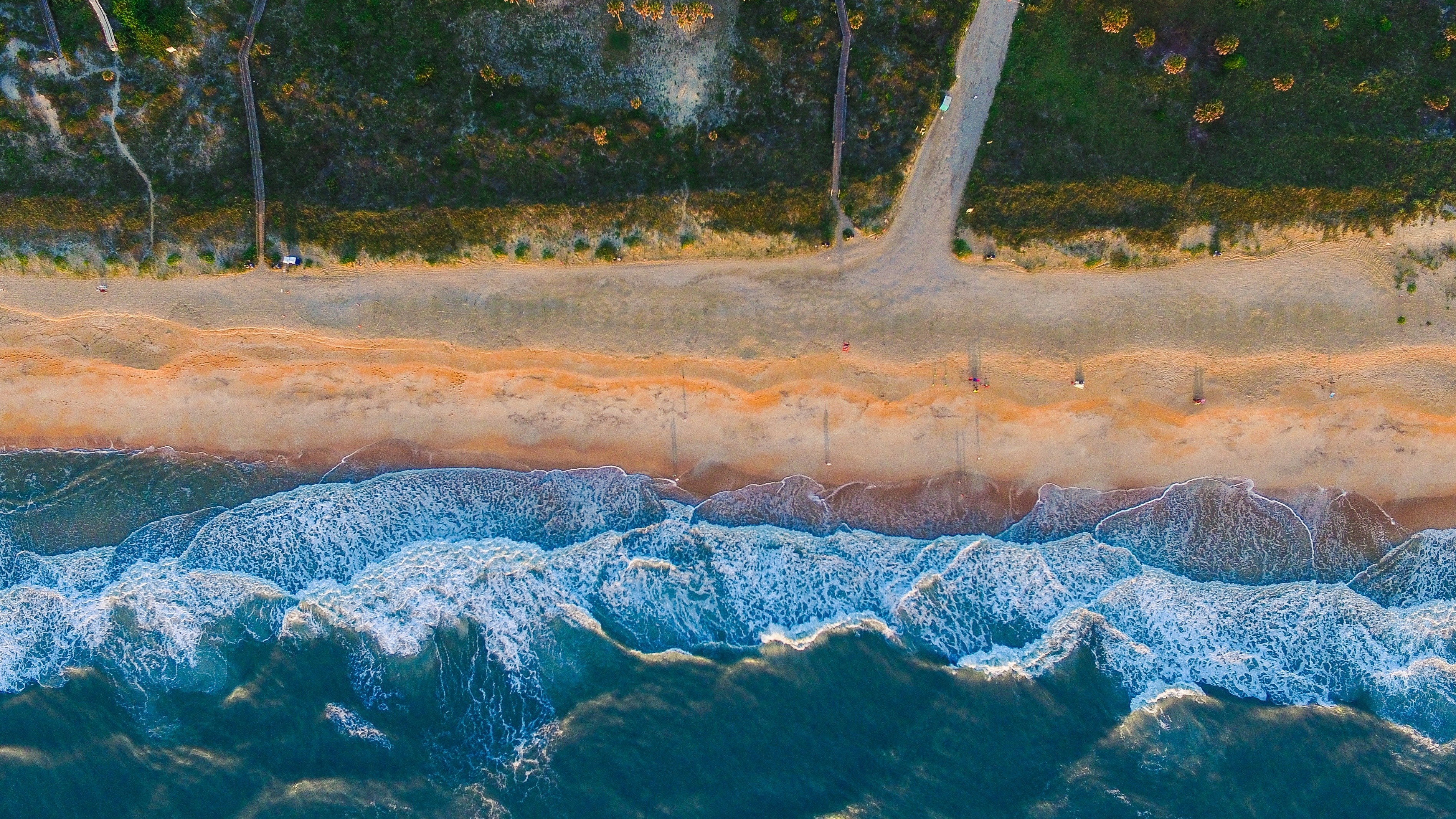 Aerial view of a sandy beach with ocean waves HD Wallpaper