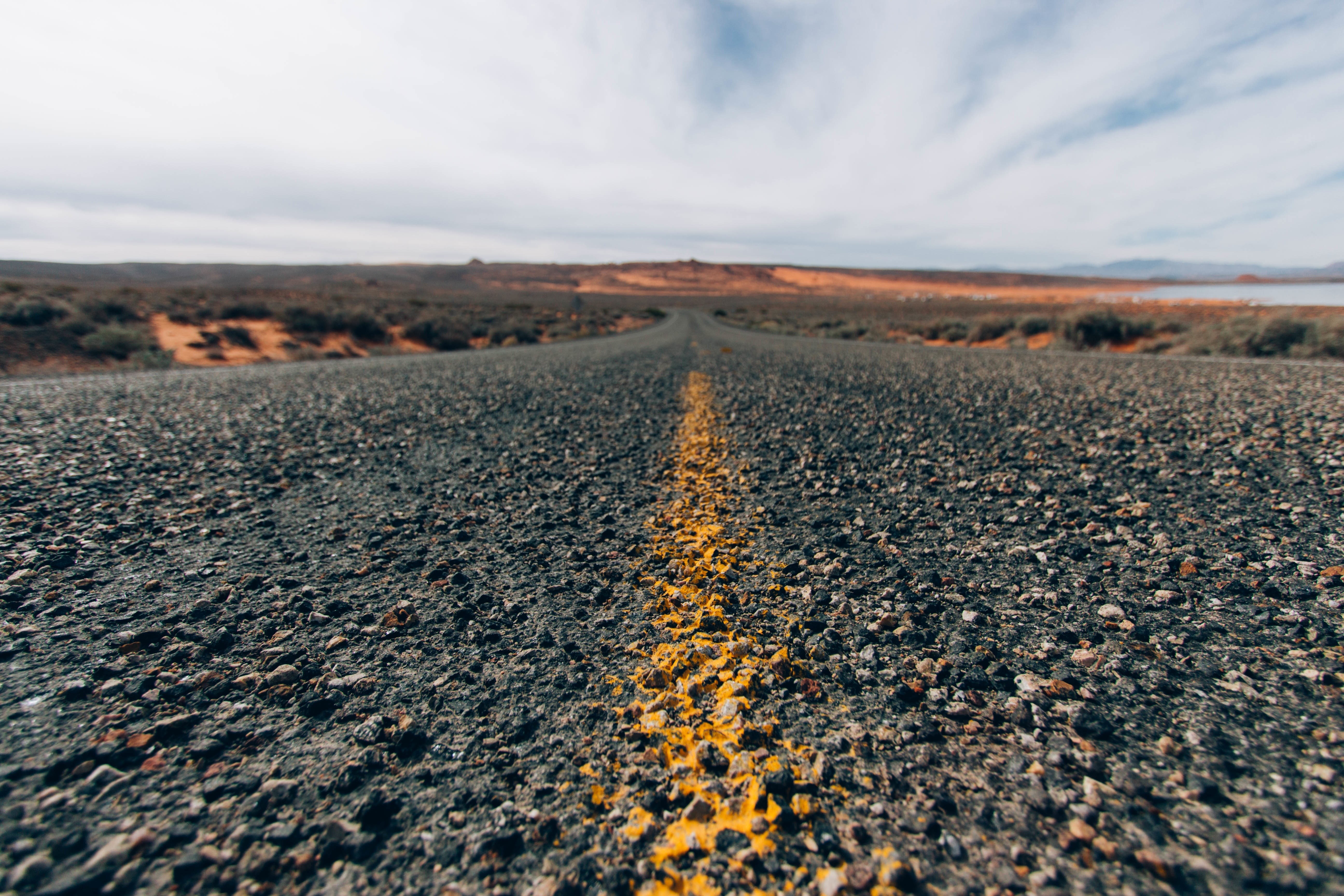 Desert road with yellow line and distant hills HD Wallpaper