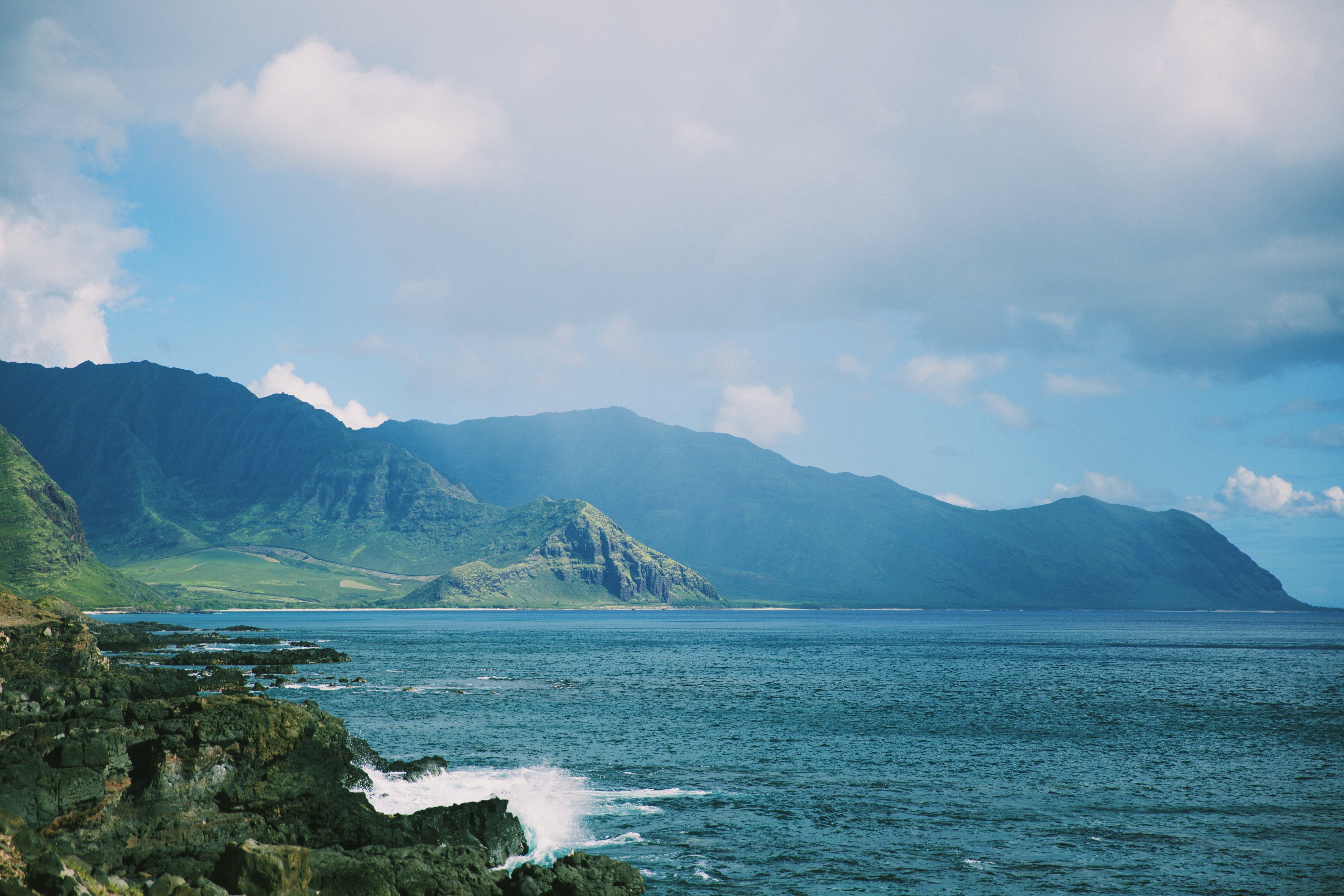 Ocean waves crash against rocky coast with mountains in background HD Wallpaper