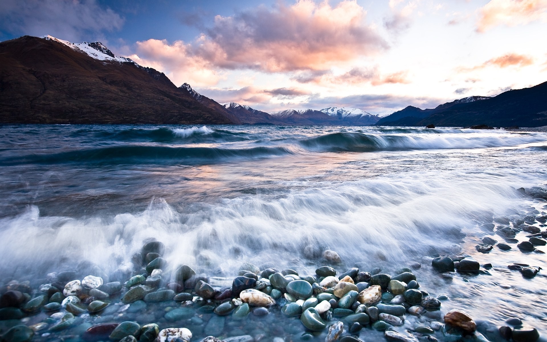 Waves crashing on a rocky shore with mountains in the background HD Wallpaper