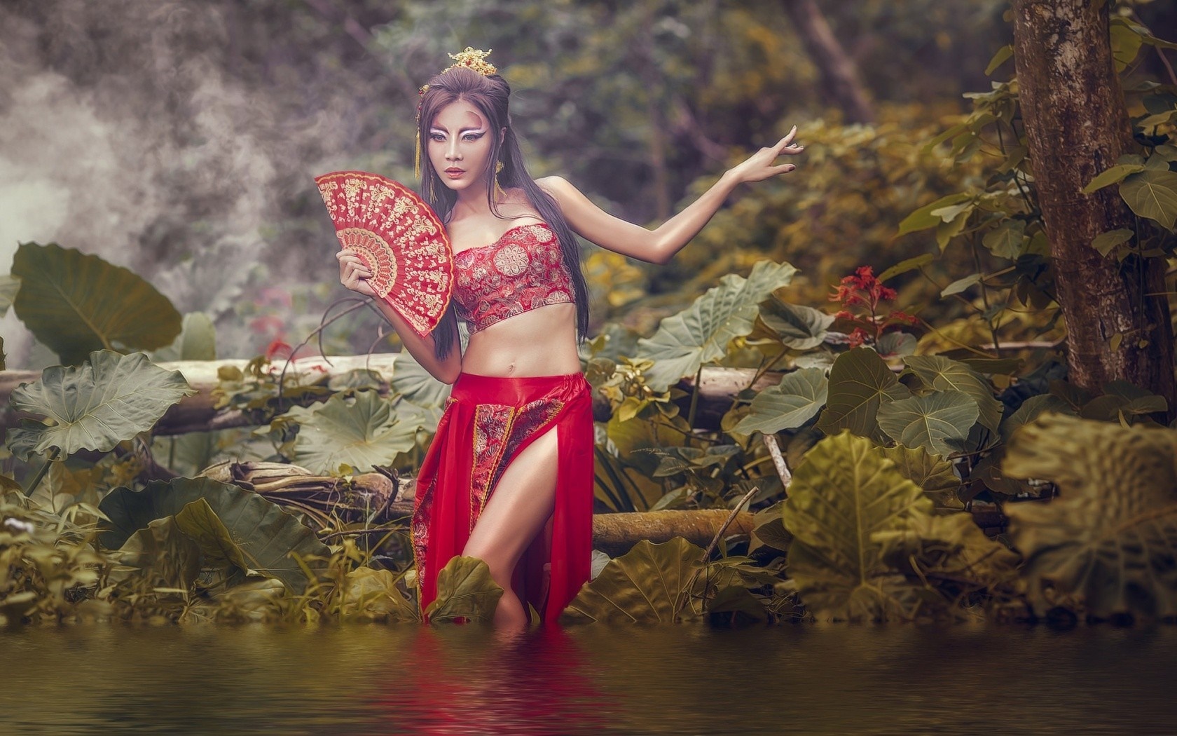 Asian woman in traditional attire holding a fan in a forest HD Wallpaper