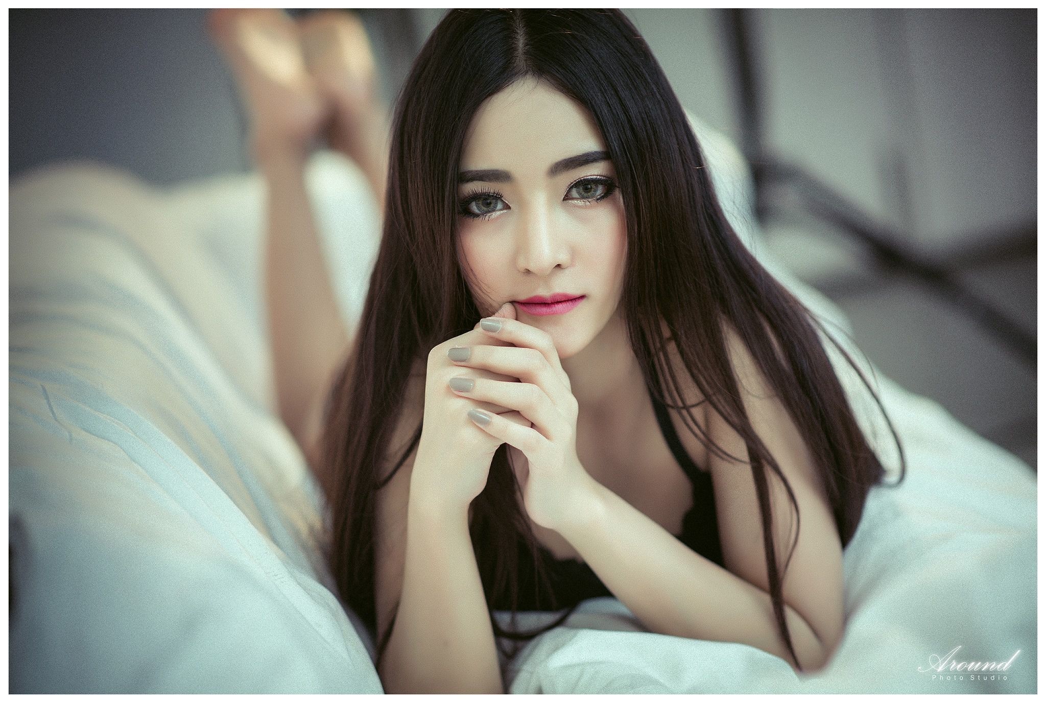Asian woman with long dark hair lying on a bed HD Wallpaper
