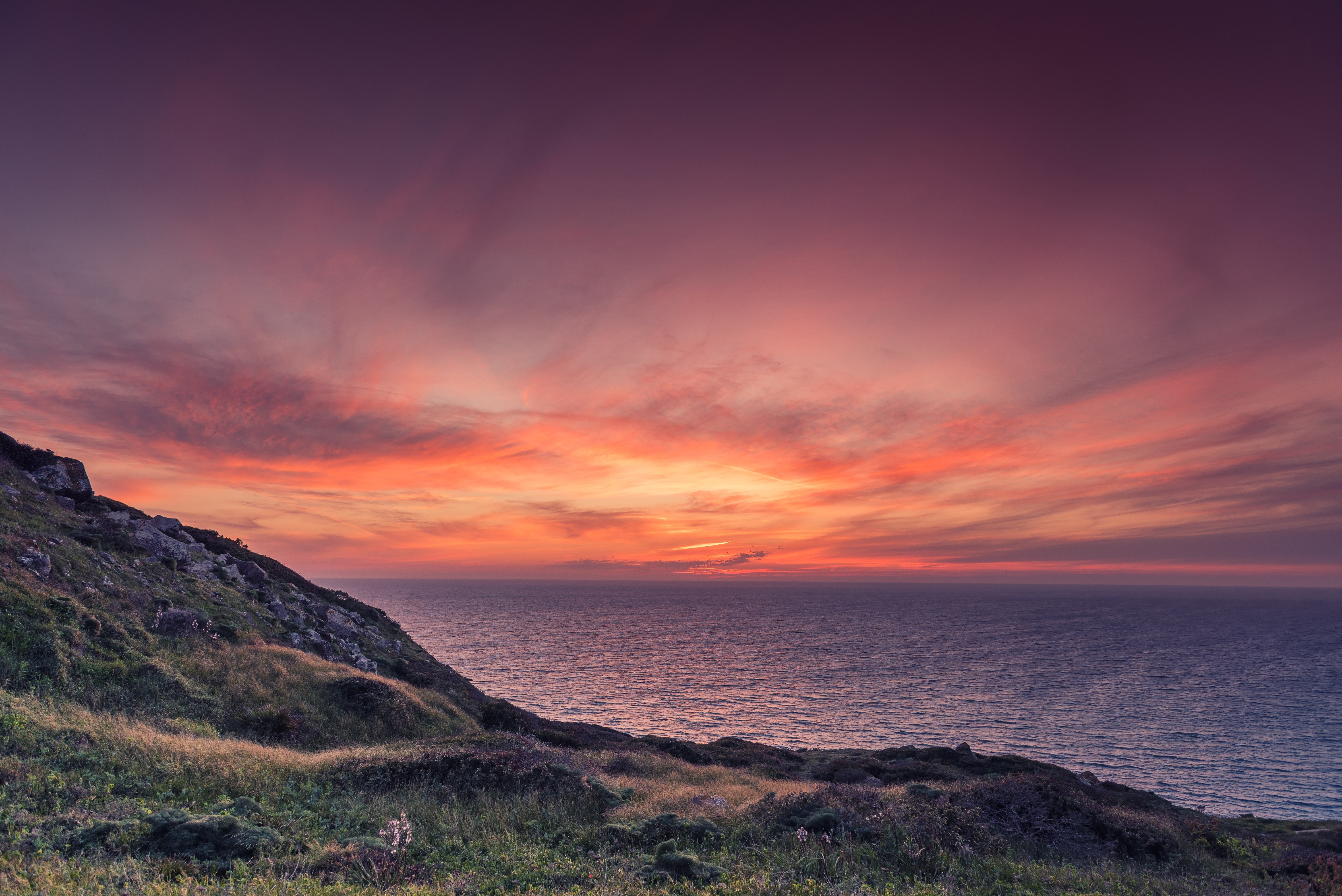 Sunset over the ocean with a grassy hill HD Wallpaper
