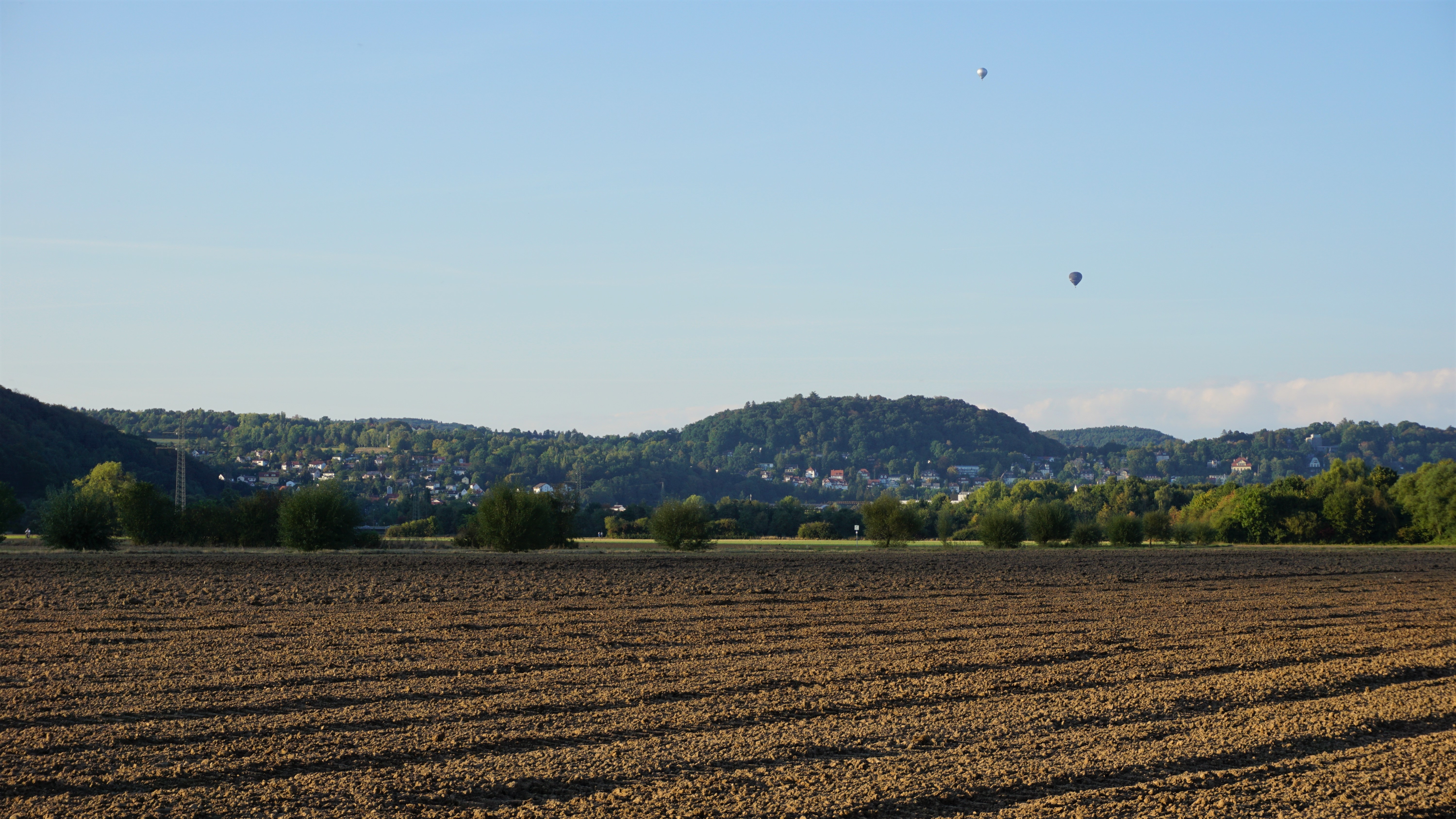 Hot air balloons over a rural landscape with a plowed field HD Wallpaper