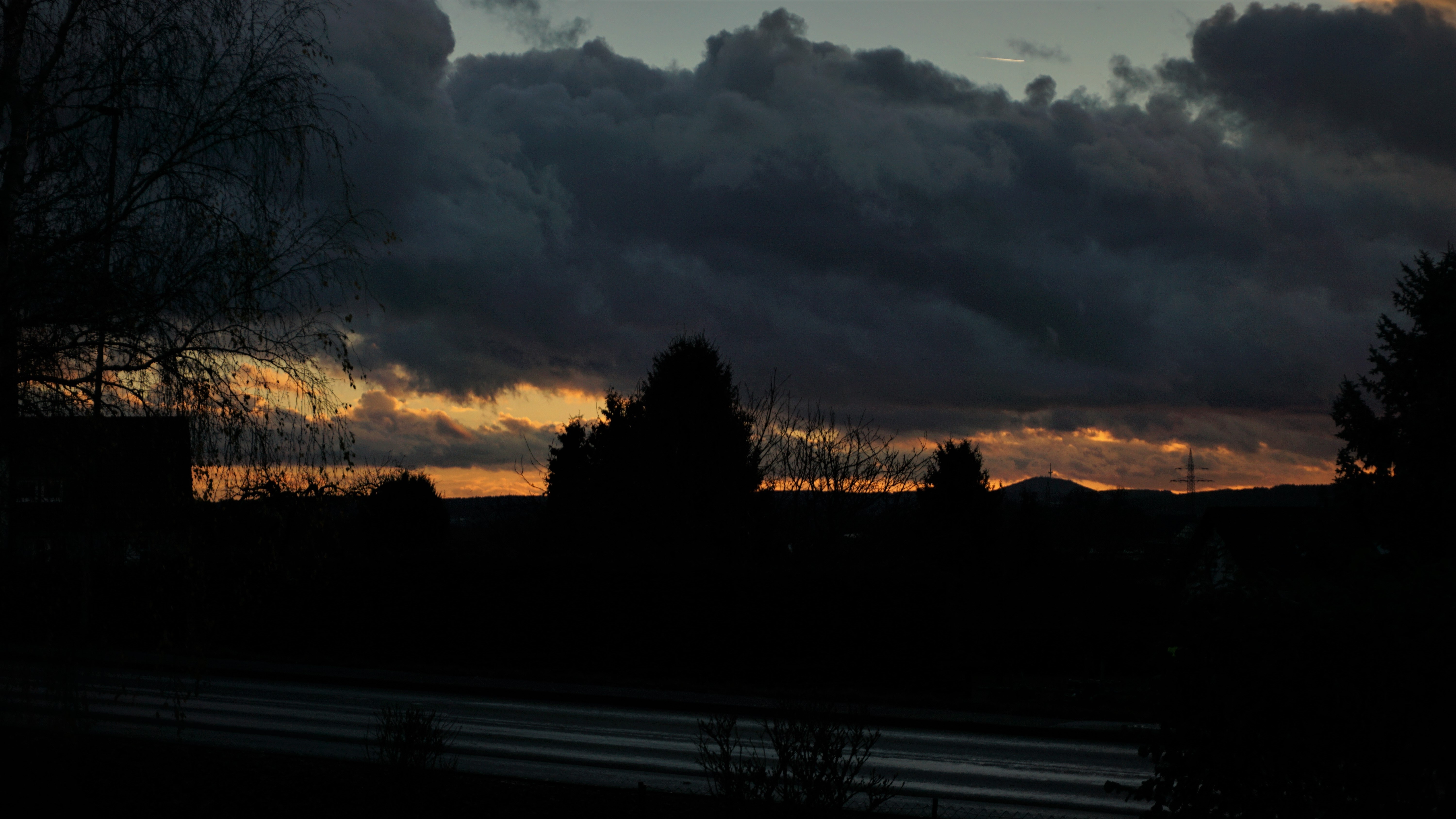 Dark clouds at sunset over a silhouetted landscape HD Wallpaper