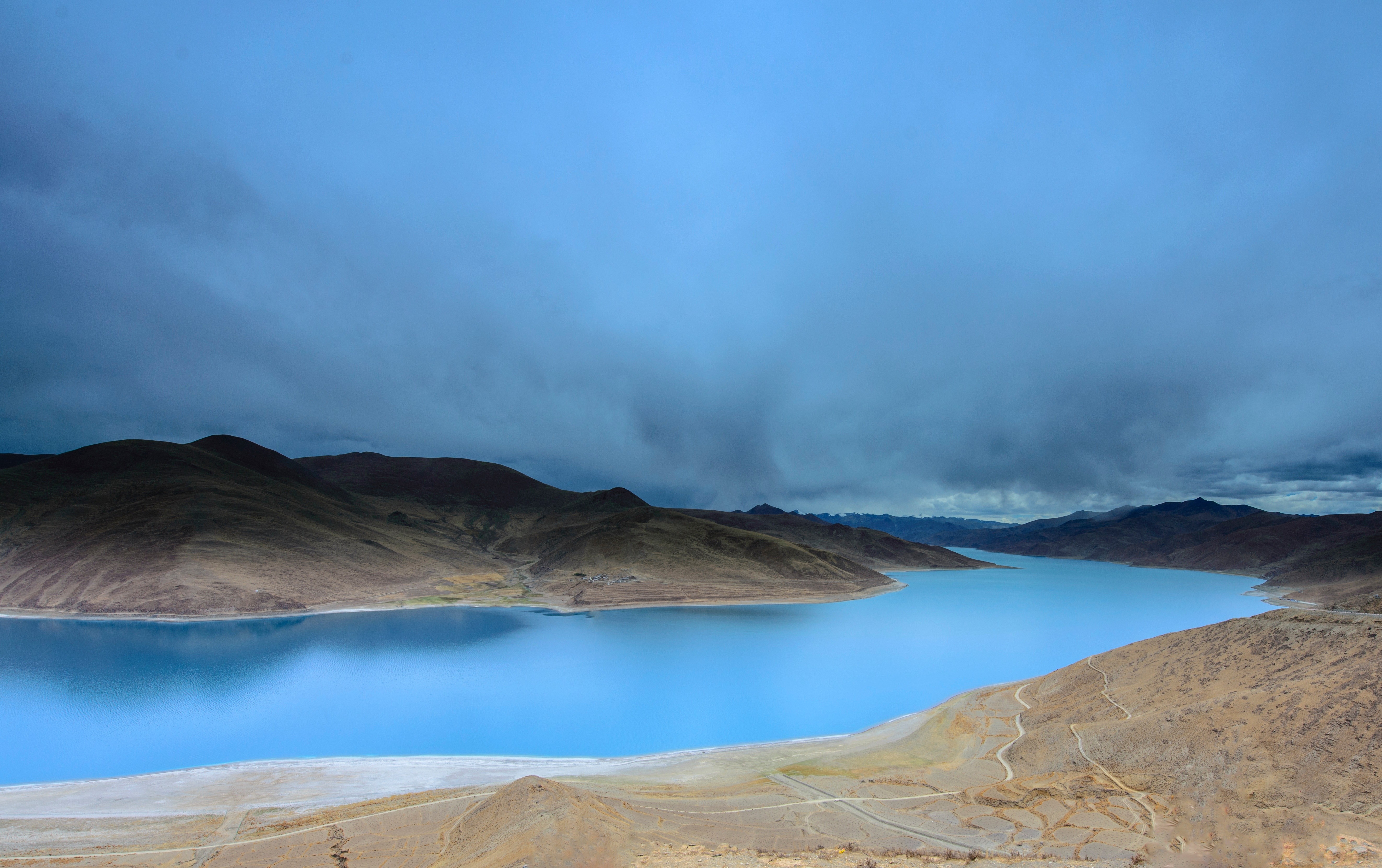Vast blue lake surrounded by barren mountains under a cloudy sky HD Wallpaper