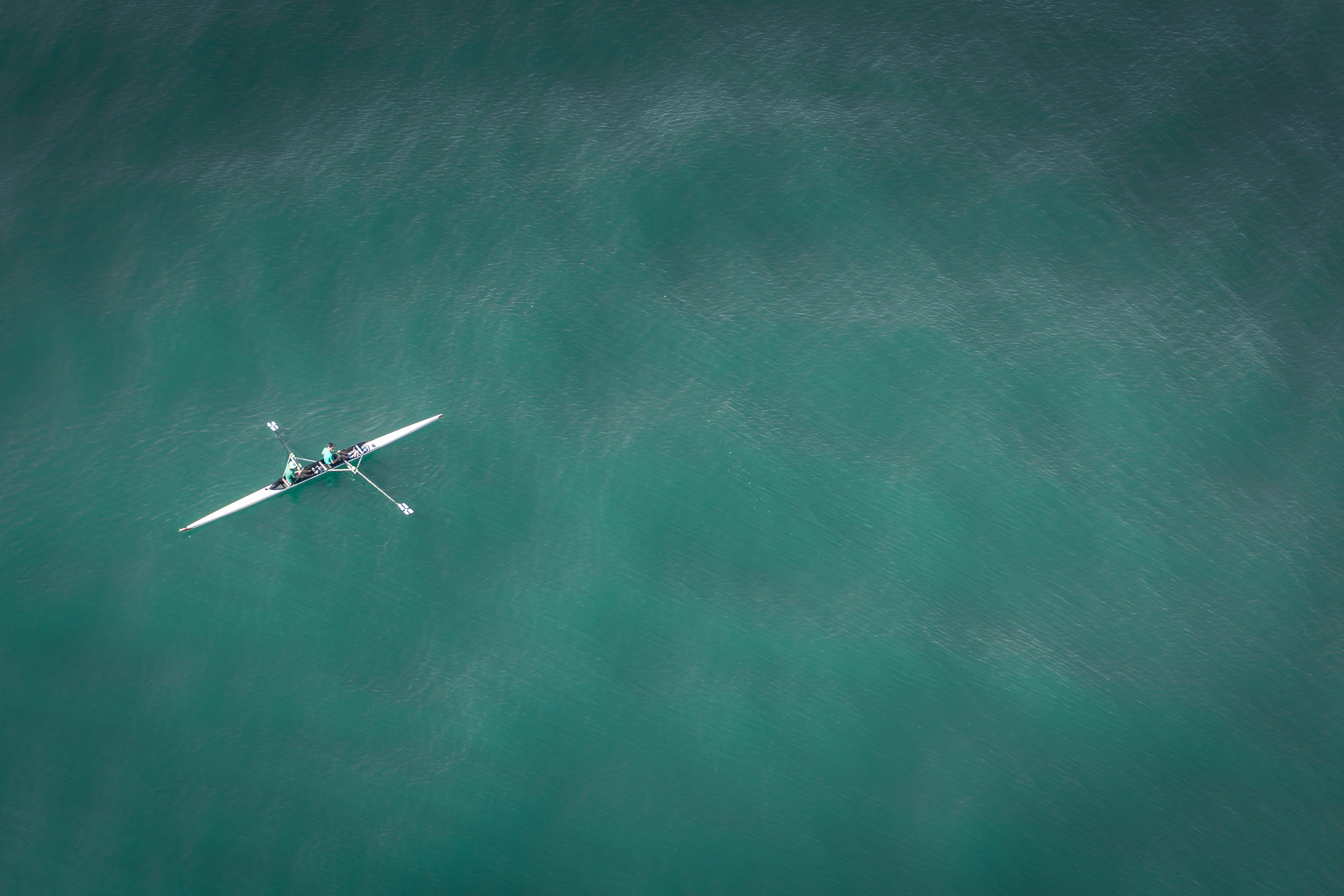 Two people rowing a white boat on a teal sea HD Wallpaper