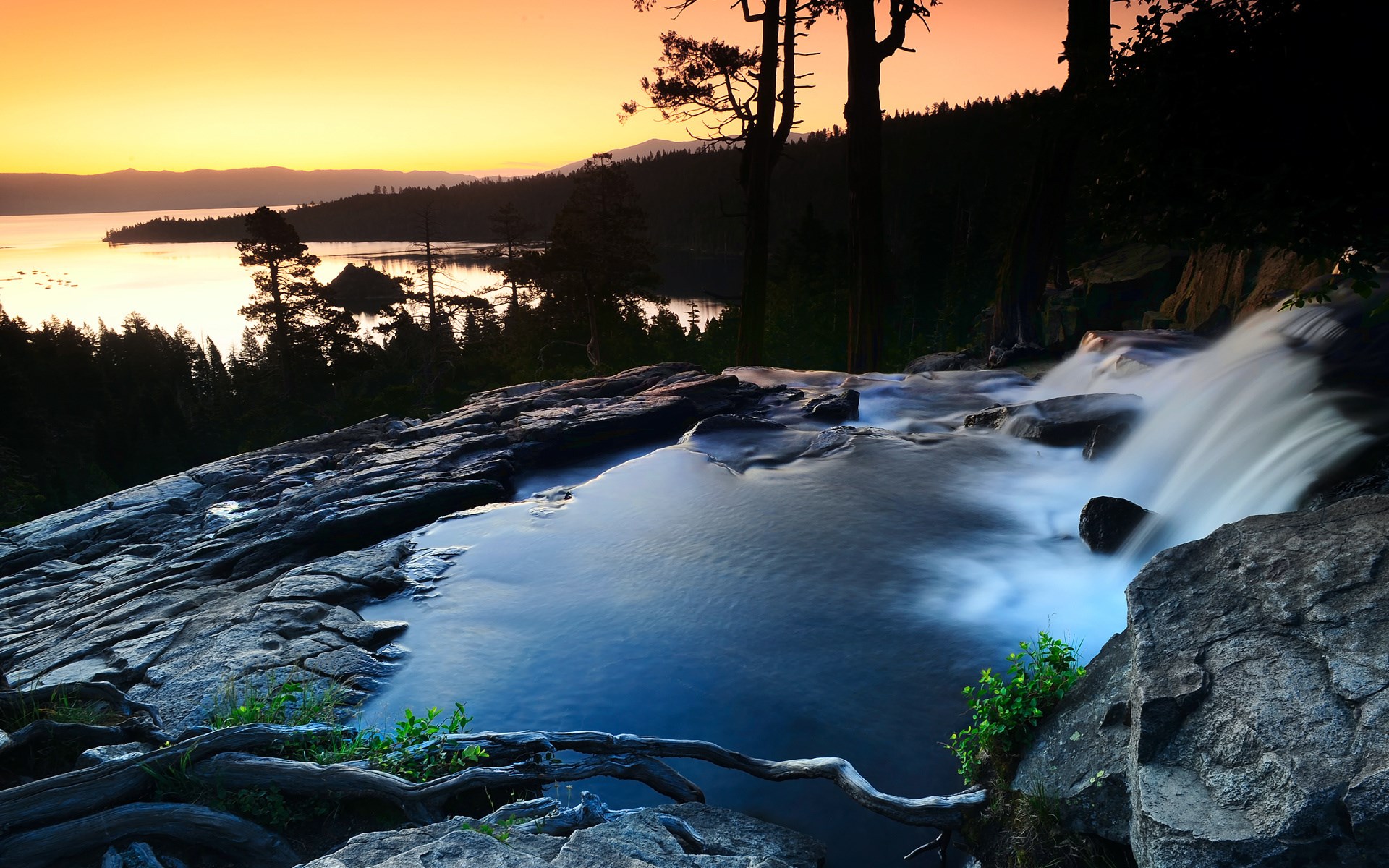 Waterfall flowing over rocks into a lake at sunset HD Wallpaper