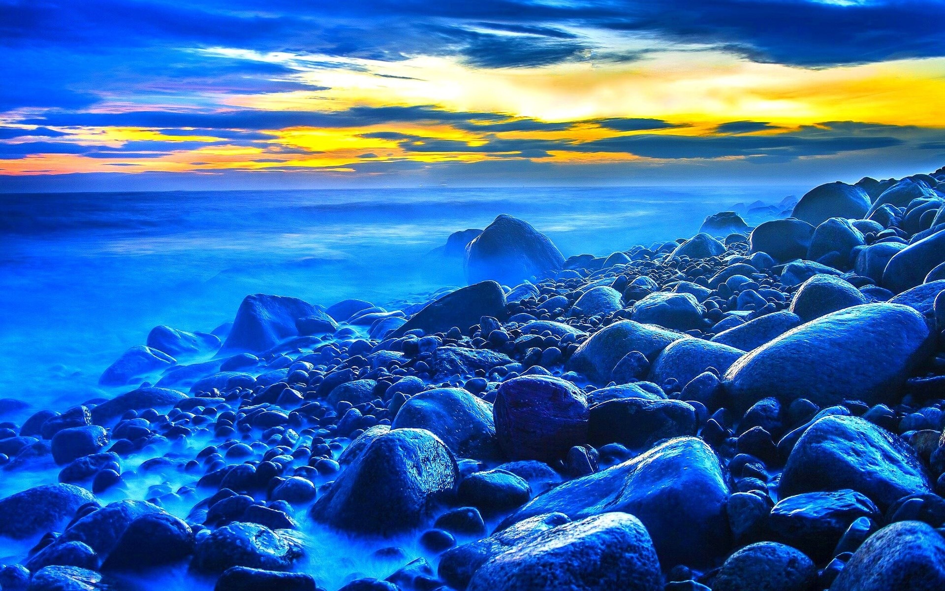 Rocky beach at sunset with blue ocean and yellow sky HD Wallpaper
