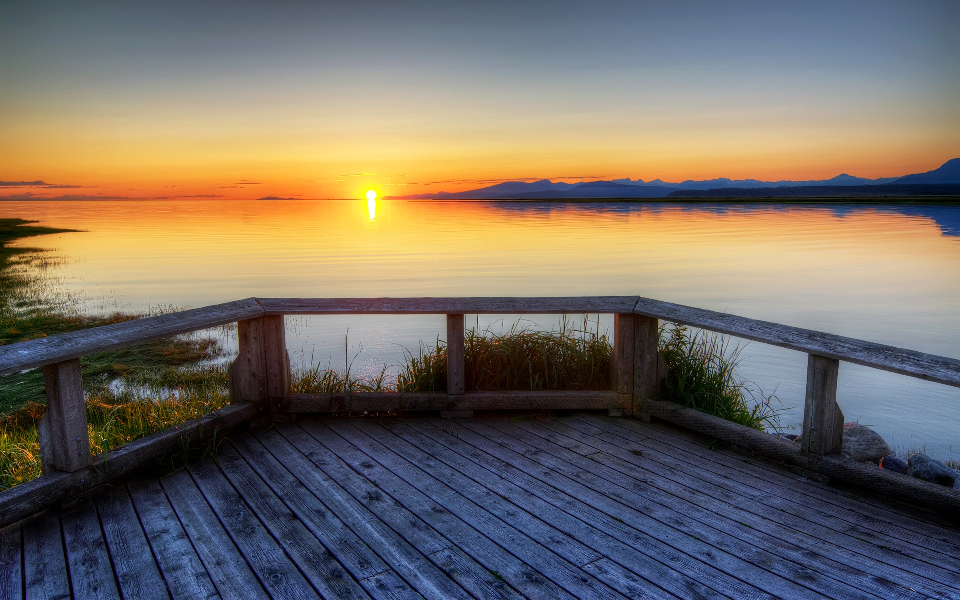 Wooden deck overlooking a calm lake at sunset HD Wallpaper